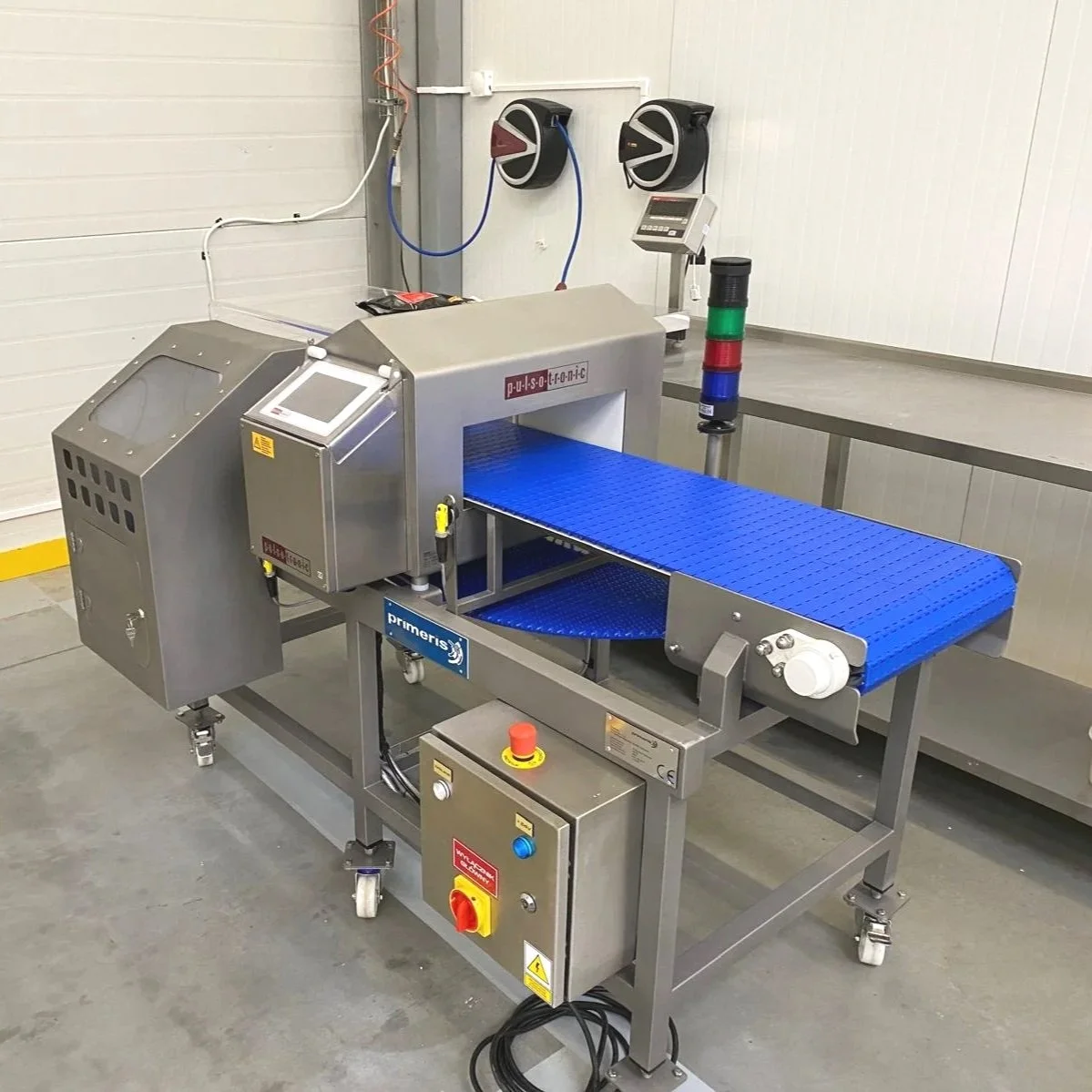 Industrial conveyor machine with blue belt, control panel, and warning lights in a manufacturing or processing facility.