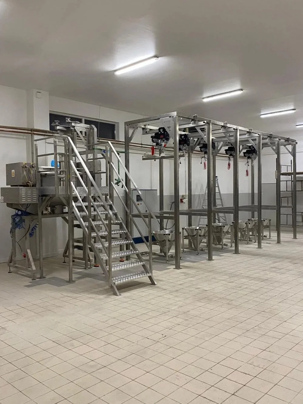 An industrial room with stainless steel equipment, metal stairs, and large piping on the ceiling.