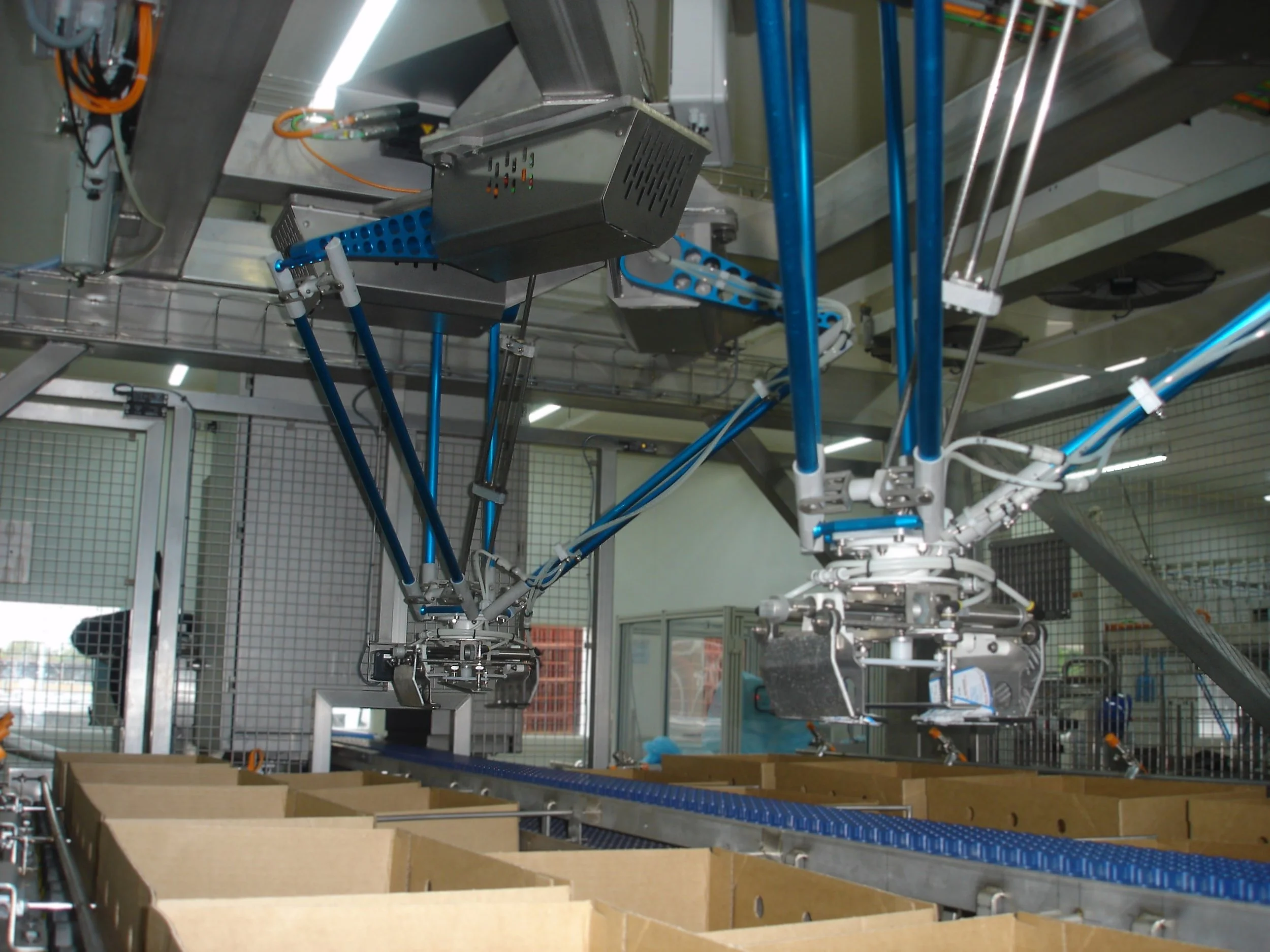 A manufacturing robot arm working on a conveyor system in an industrial setting with cardboard boxes.