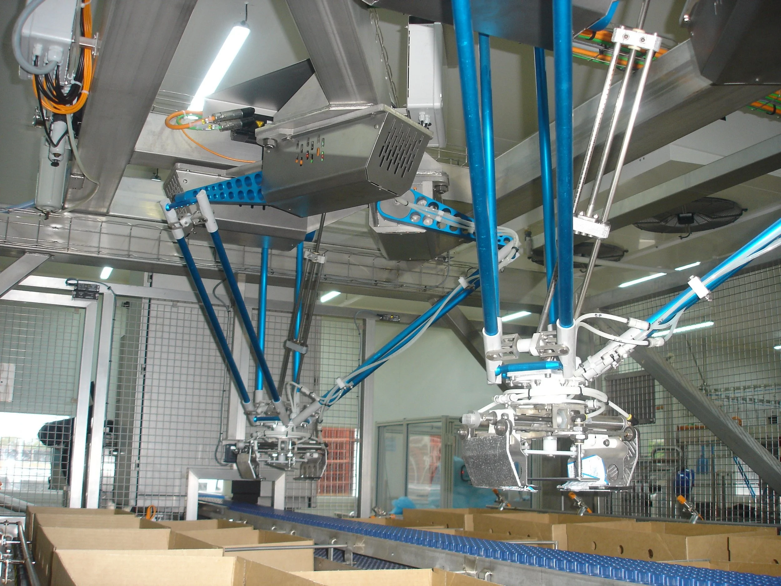 An industrial robotic arm operating in a manufacturing or packaging facility, handling boxes on a conveyor belt.