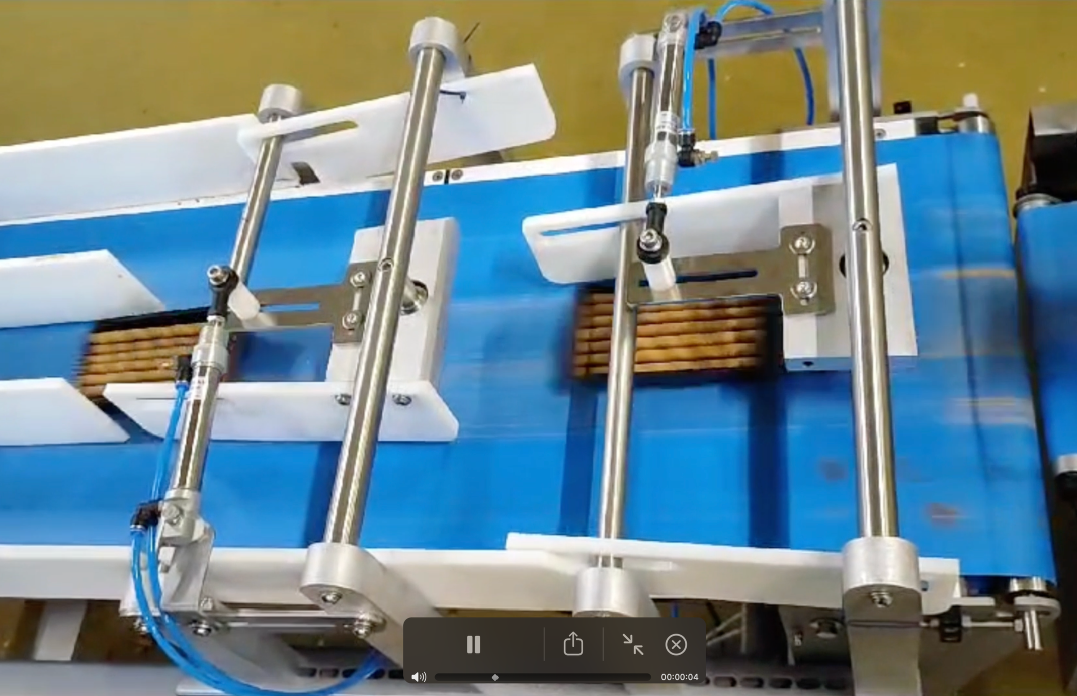 Close-up of a mechanical device with blue and white parts, metal rods and adjustable components, possibly part of a robot or manufacturing equipment, on a yellow surface.