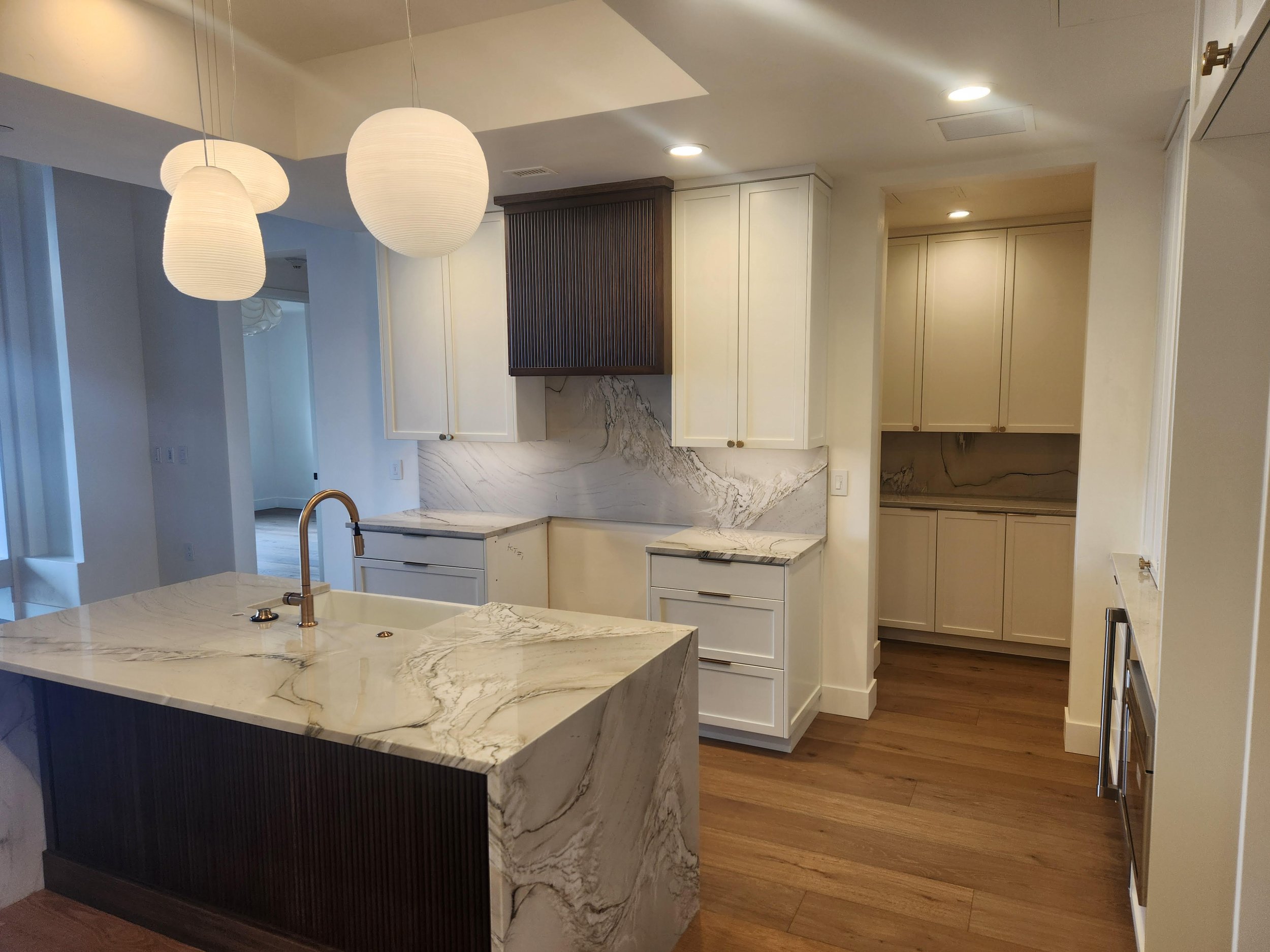 Modern kitchen with marble countertops, white cabinetry, pendant lights, and hardwood floors.