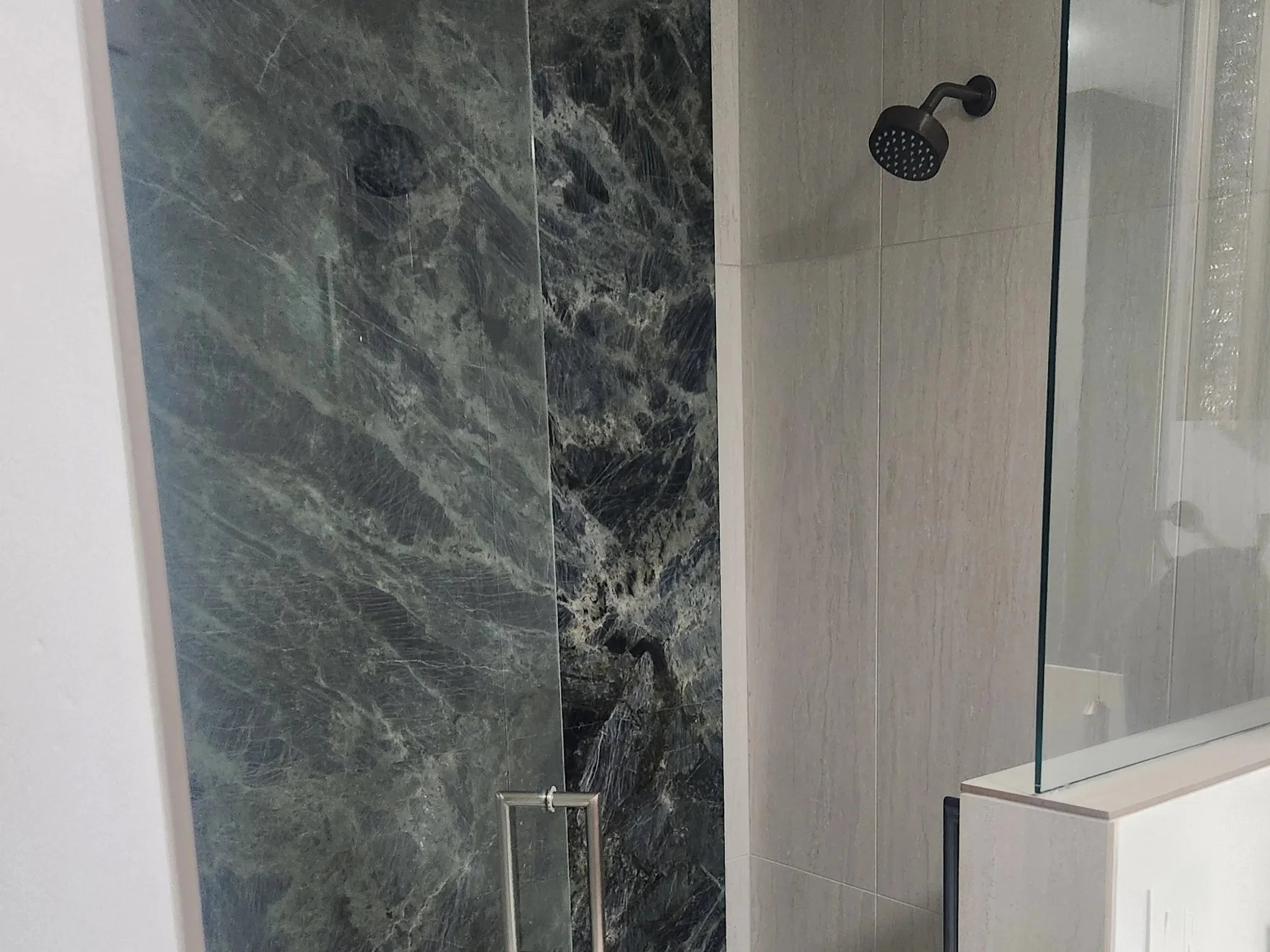 A modern shower with dark gray marble walls, a black showerhead, and a glass door.