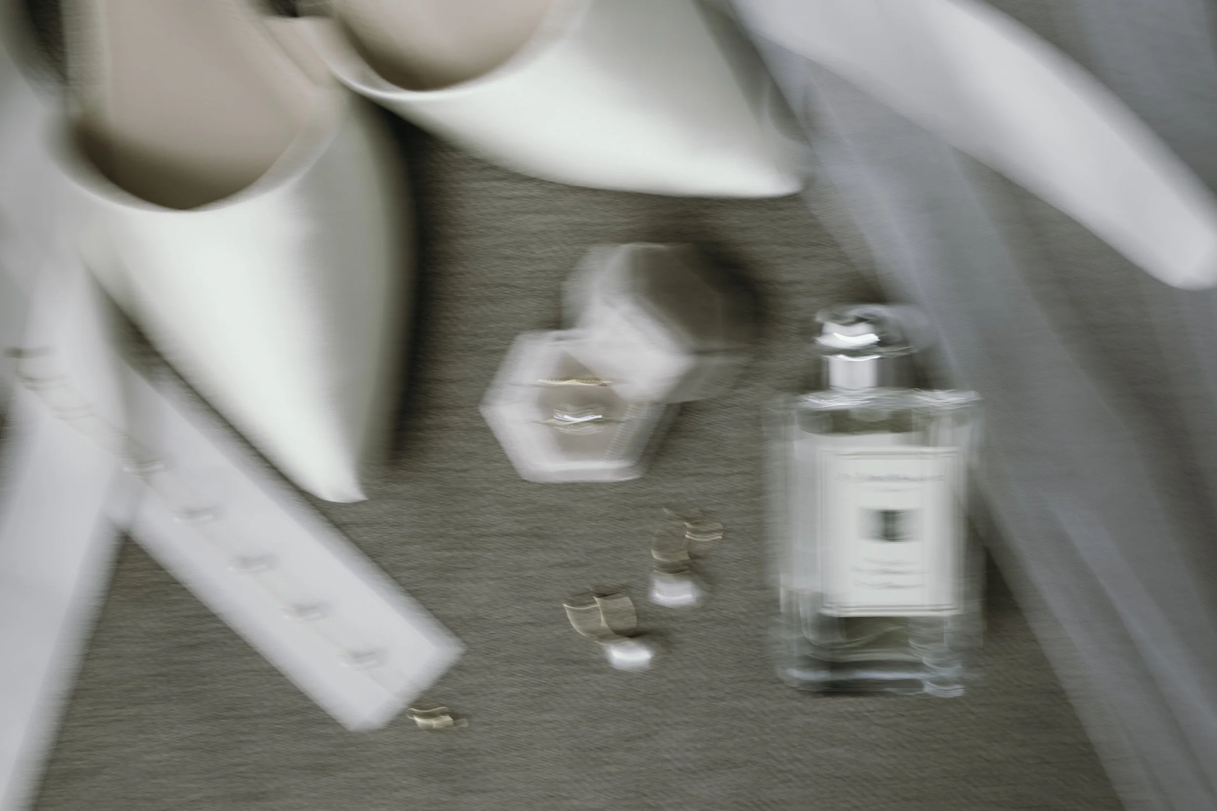 Blurry image showing two white cups, a white rectangle object, a small perfume bottle, a hexagonal container, and a rectangular box on a gray surface.