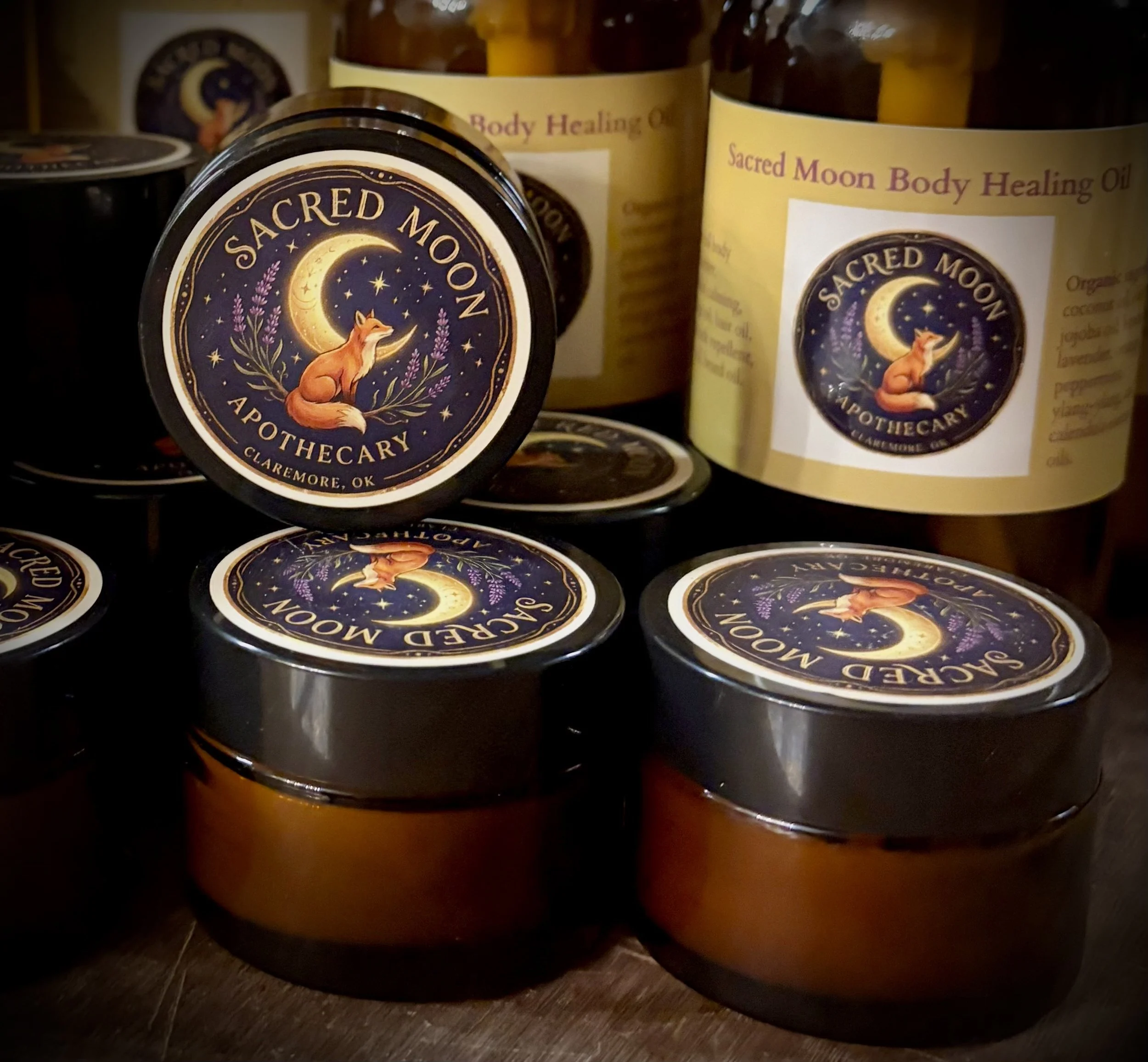 Containers of Sacred Moon Apothecary Sacred Moon Body Healing Oil with a label featuring a fox sitting under a crescent moon surrounded by stars and lavender.