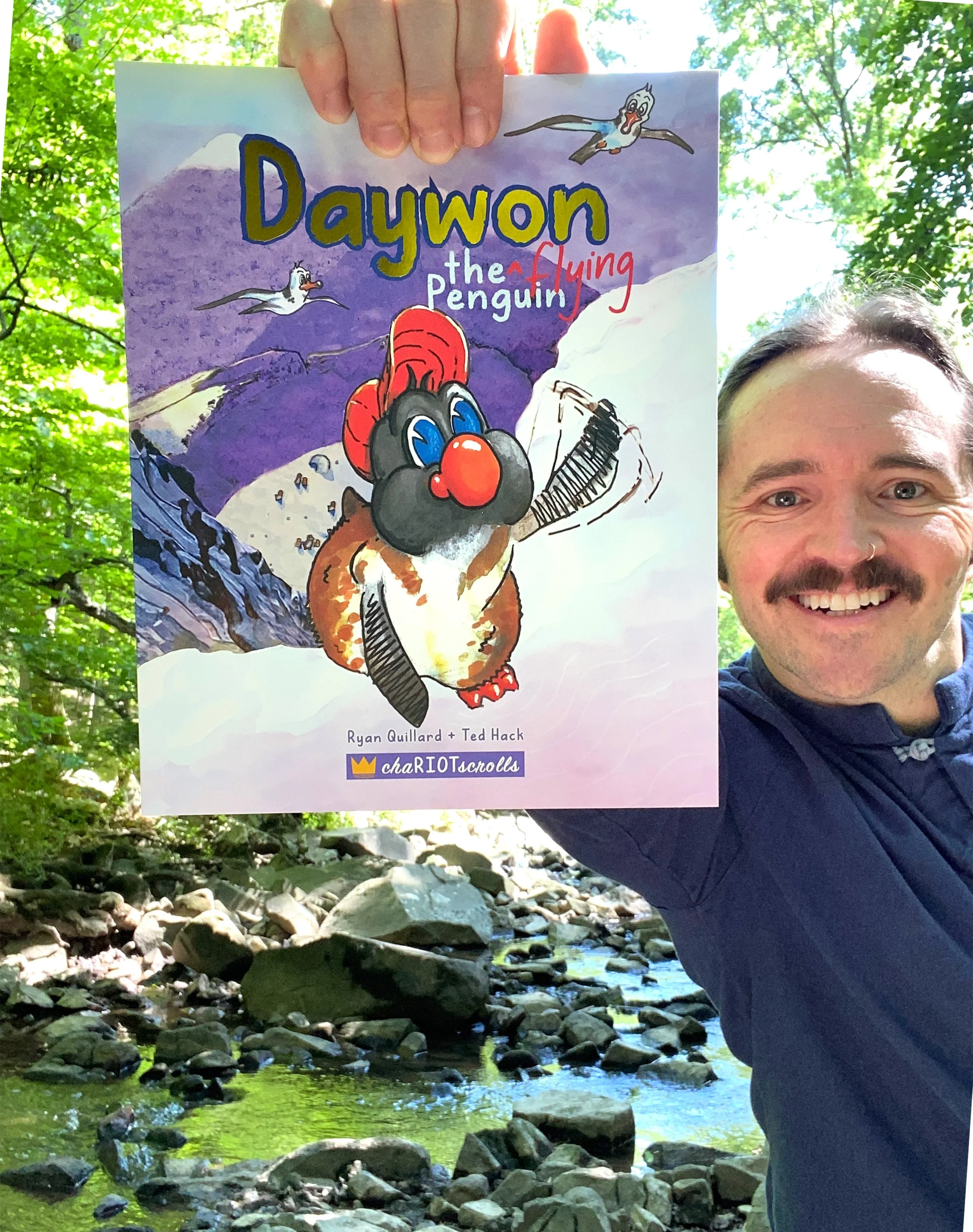 Author Ryan Quillard smiling outdoors in a forest creek, holding debut book "Daywon the Flying Penguin" by Ryan Quillard and Ted Hack.