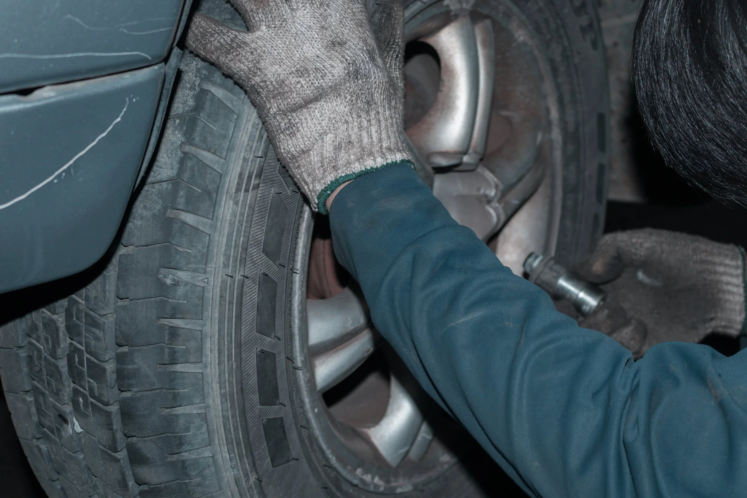 A mechanic wearing gloves working on a car wheel, possibly changing or repairing the tire.