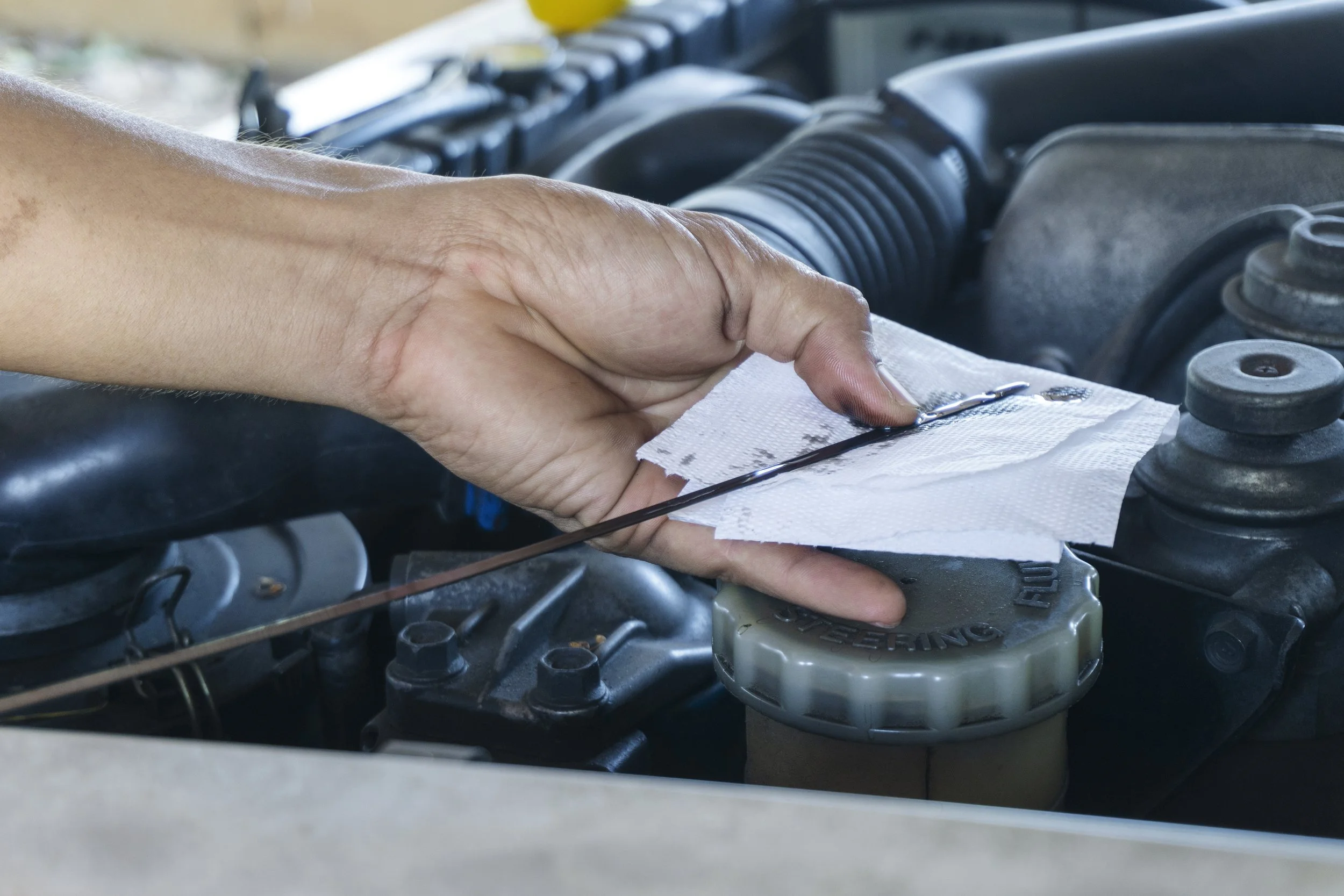 Person checking or refilling engine oil in a car engine using a mechanic's tool on a paper towel.