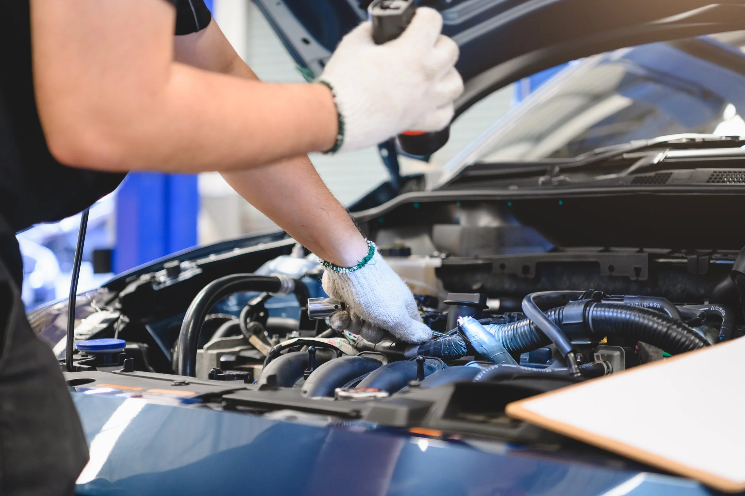 Mechanic wearing gloves working on a car engine with various engine components visible.