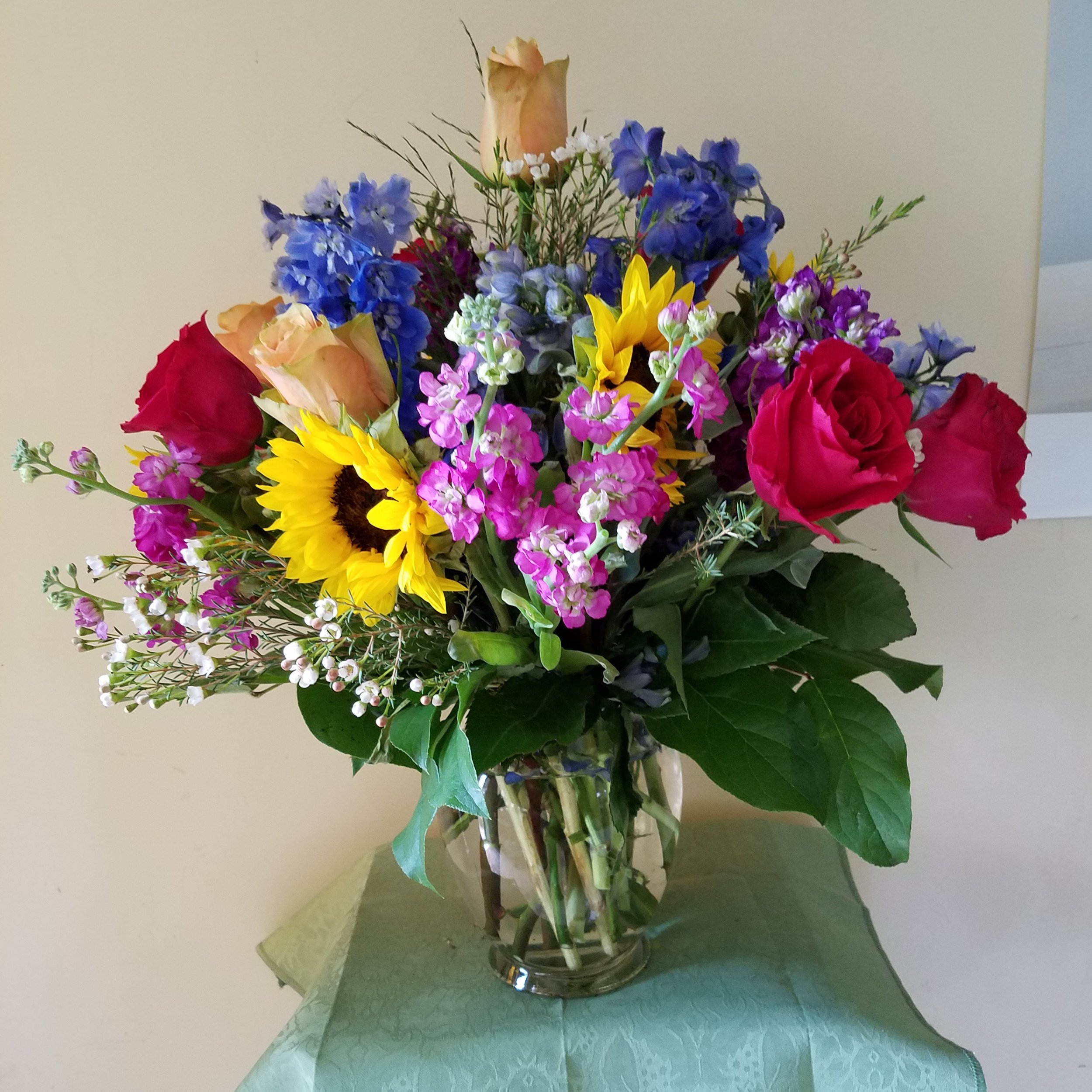 Colorful flower bouquet in a glass vase on a table, with a beige and white background.