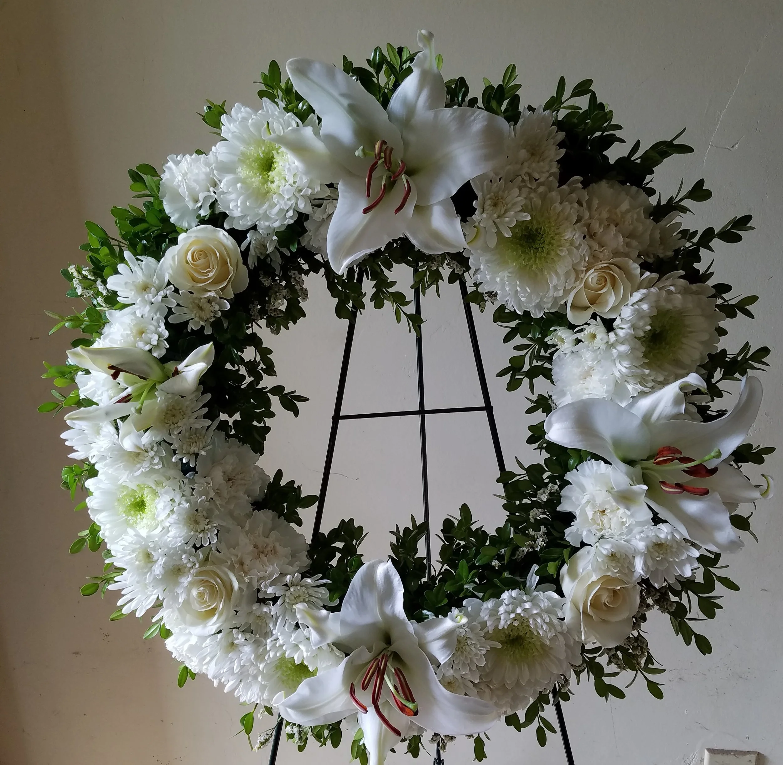 Arrangement of white lilies, roses, and chrysanthemums with green leaves on a stand.
