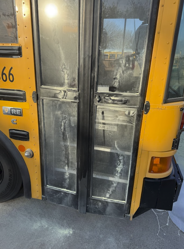 Front door of a yellow school bus with visible dirt and grime on the glass and metal surfaces.