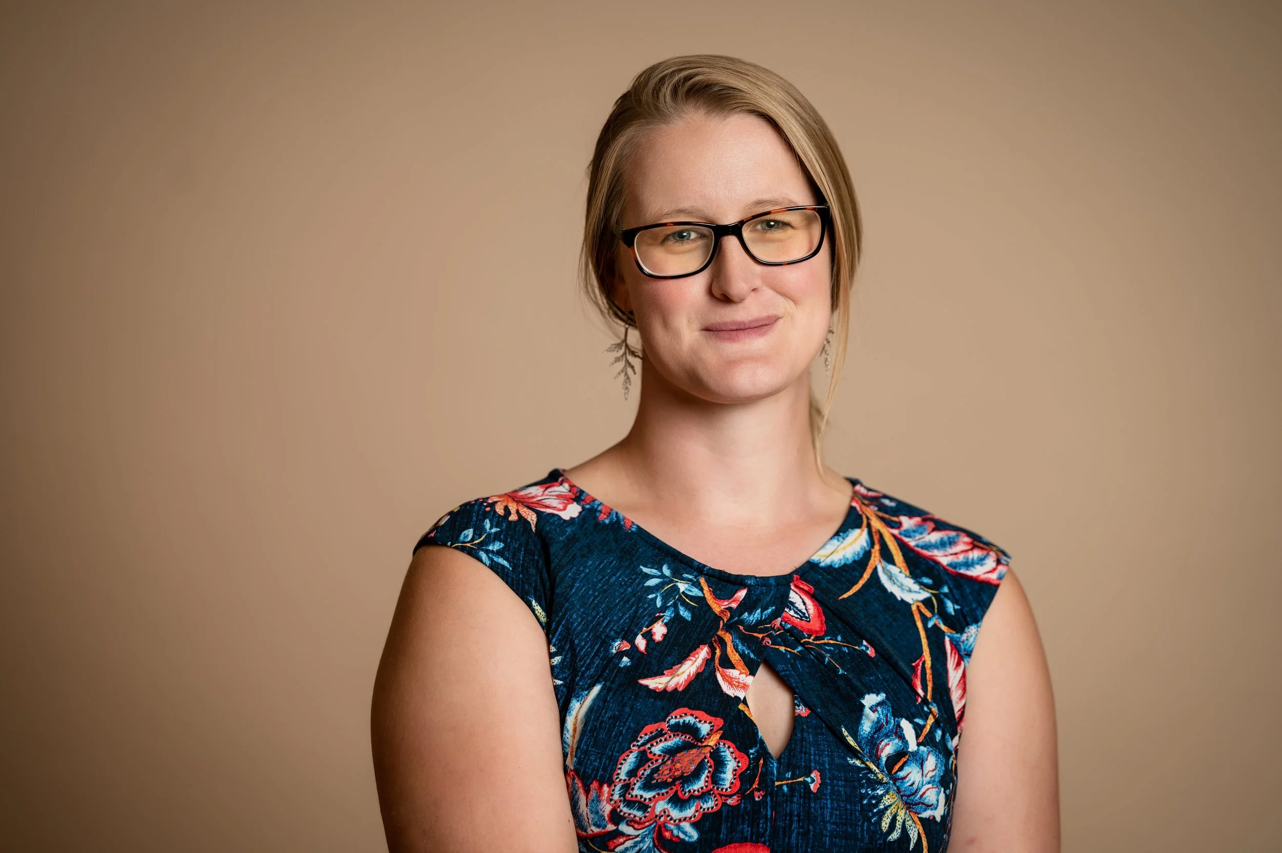 Image of Helen West - a white woman with blond hair and glasses. She is wearing a blue dress and silver earings.