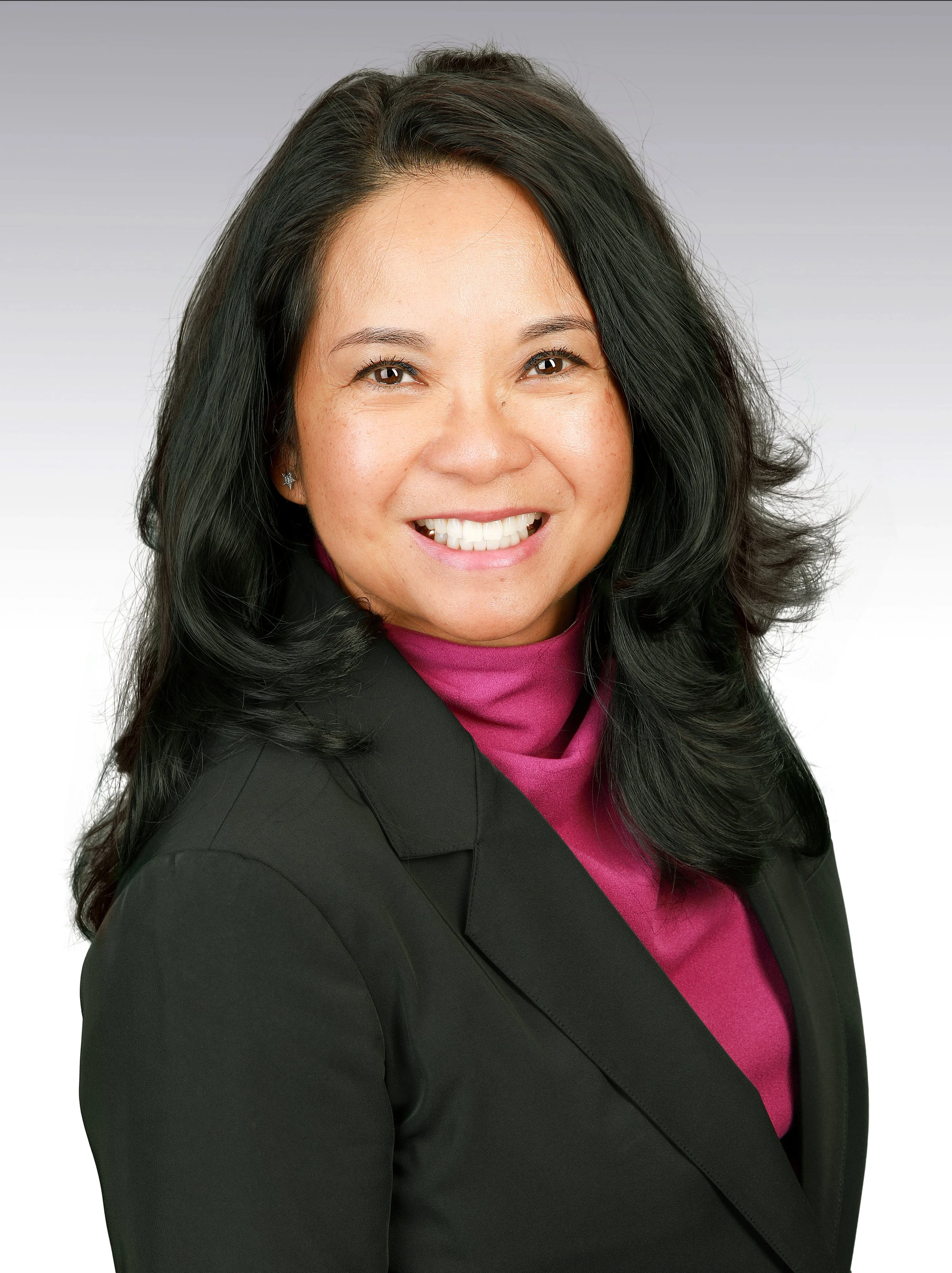 Professional woman with black hair styled in loose waves, wearing a black blazer over a magenta blouse, smiling against a neutral background.