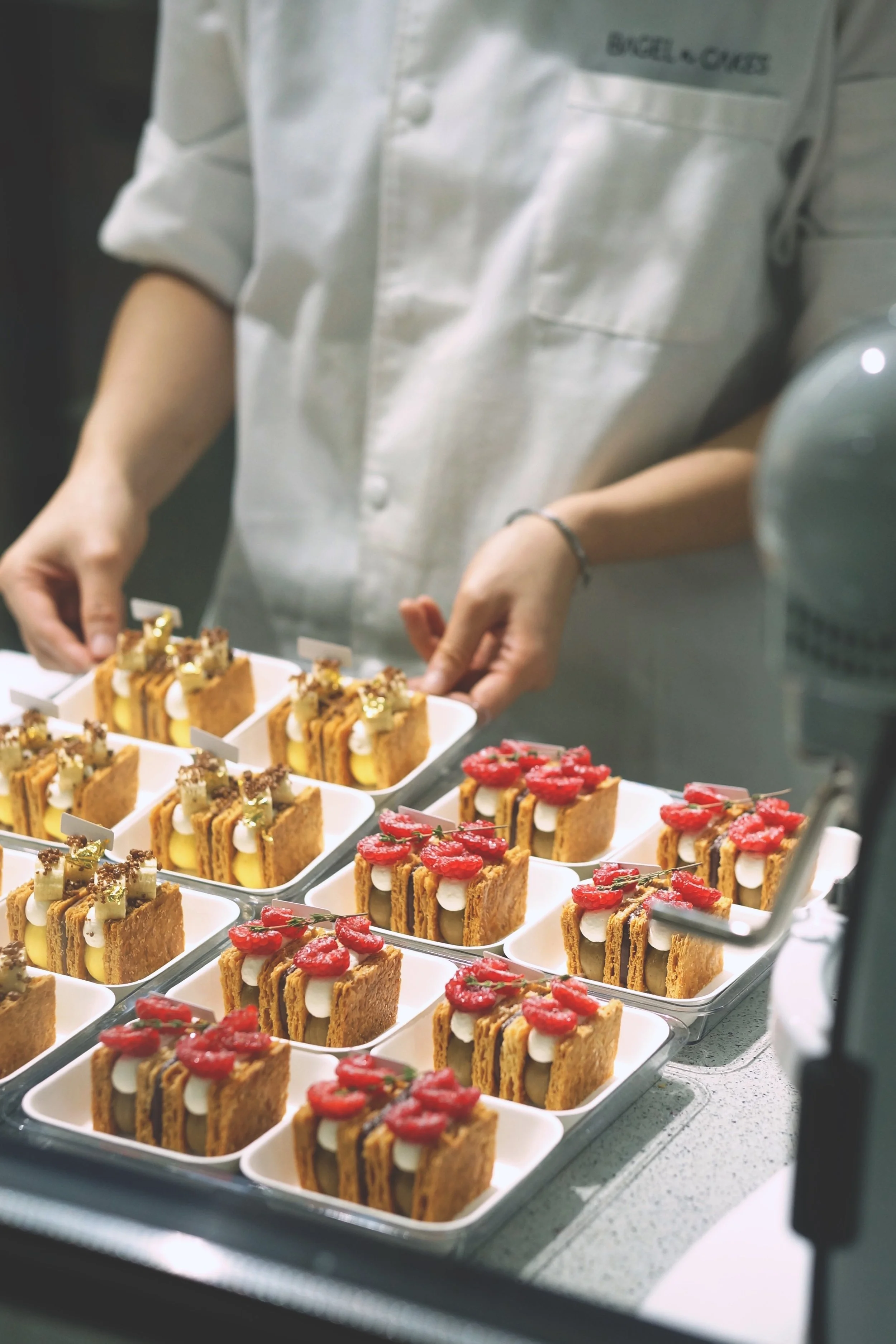 A pastry chef arranging small mille feuille with cream and fresh fruits on a kitchen counter