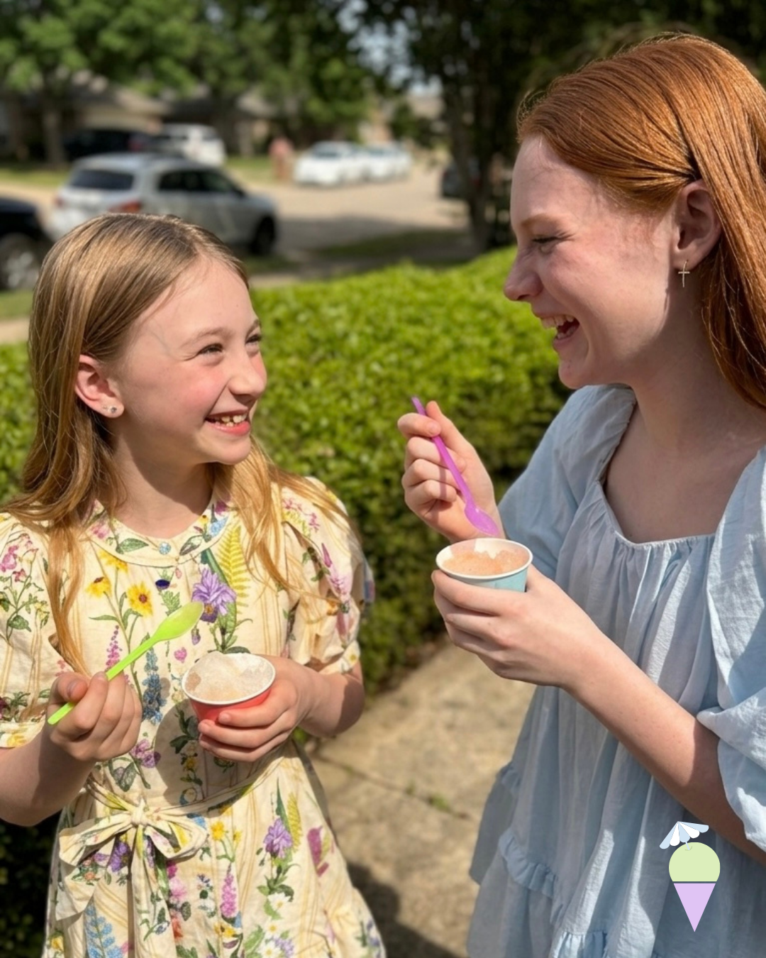two young girls, one blonde, one red head, laughing at eachother eating dye freesnowcones