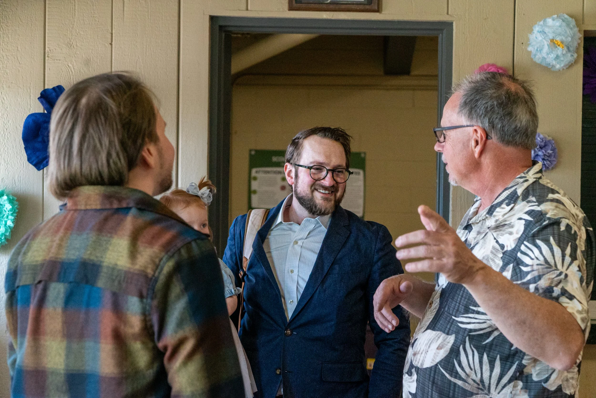 Four people engaged in conversation indoors, with decorative paper flowers on the wall.