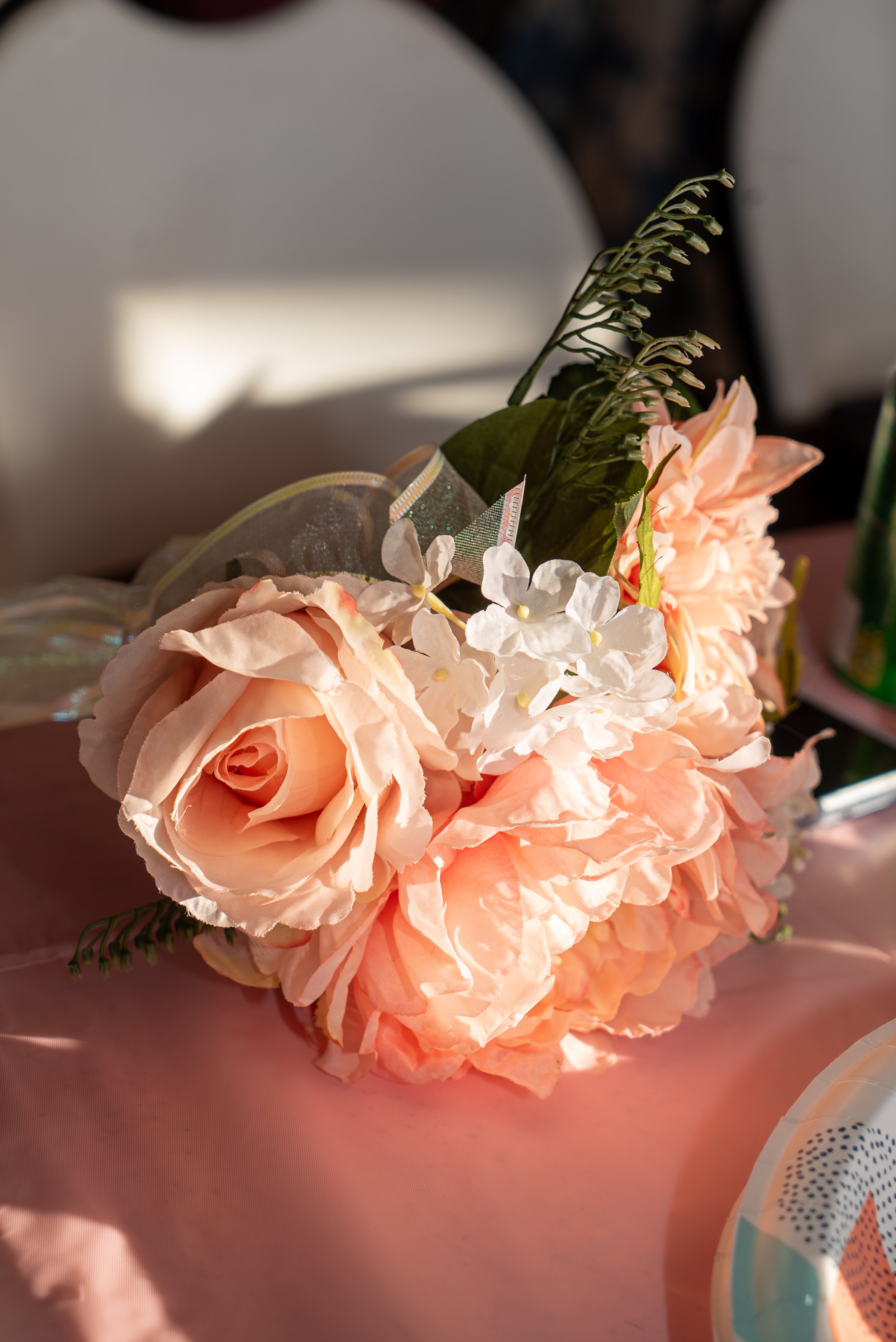 A close-up of a bouquet of artificial flowers, including pink roses, white hydrangeas, and greenery, with a slightly blurred background.