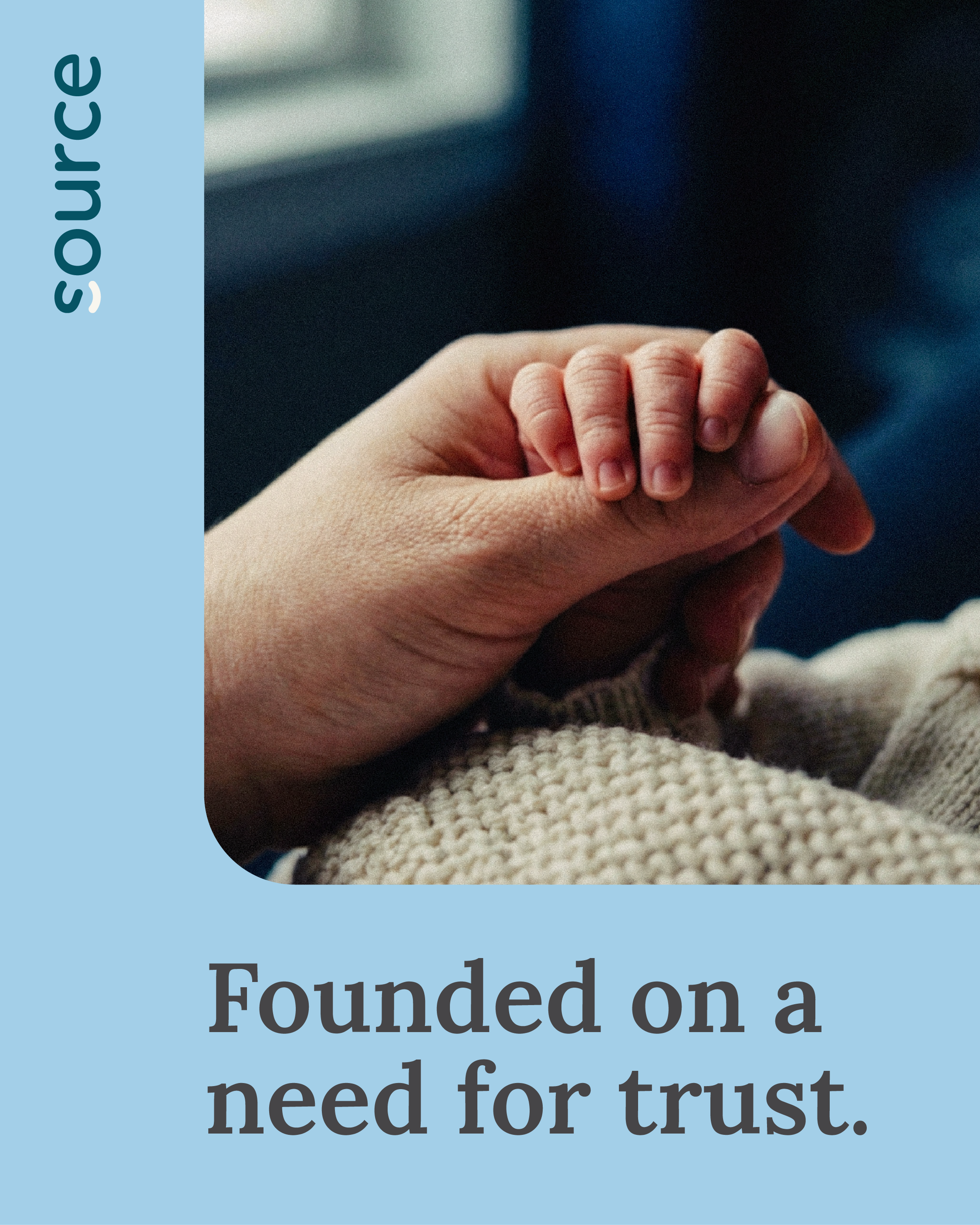 A close-up of an adult's hand holding a baby's hand, with both resting on a knitted blanket. The background is blurred.