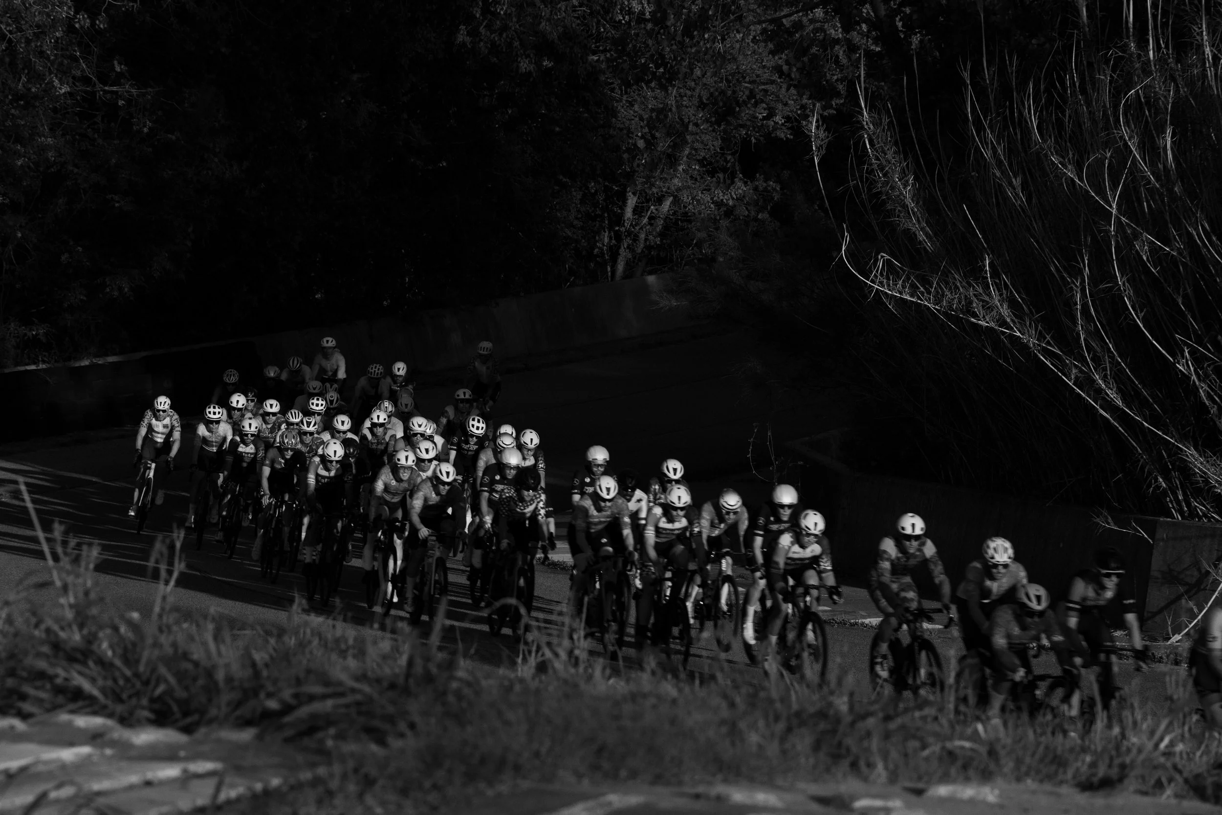 A large group of cyclists wearing helmets riding on a road at night.