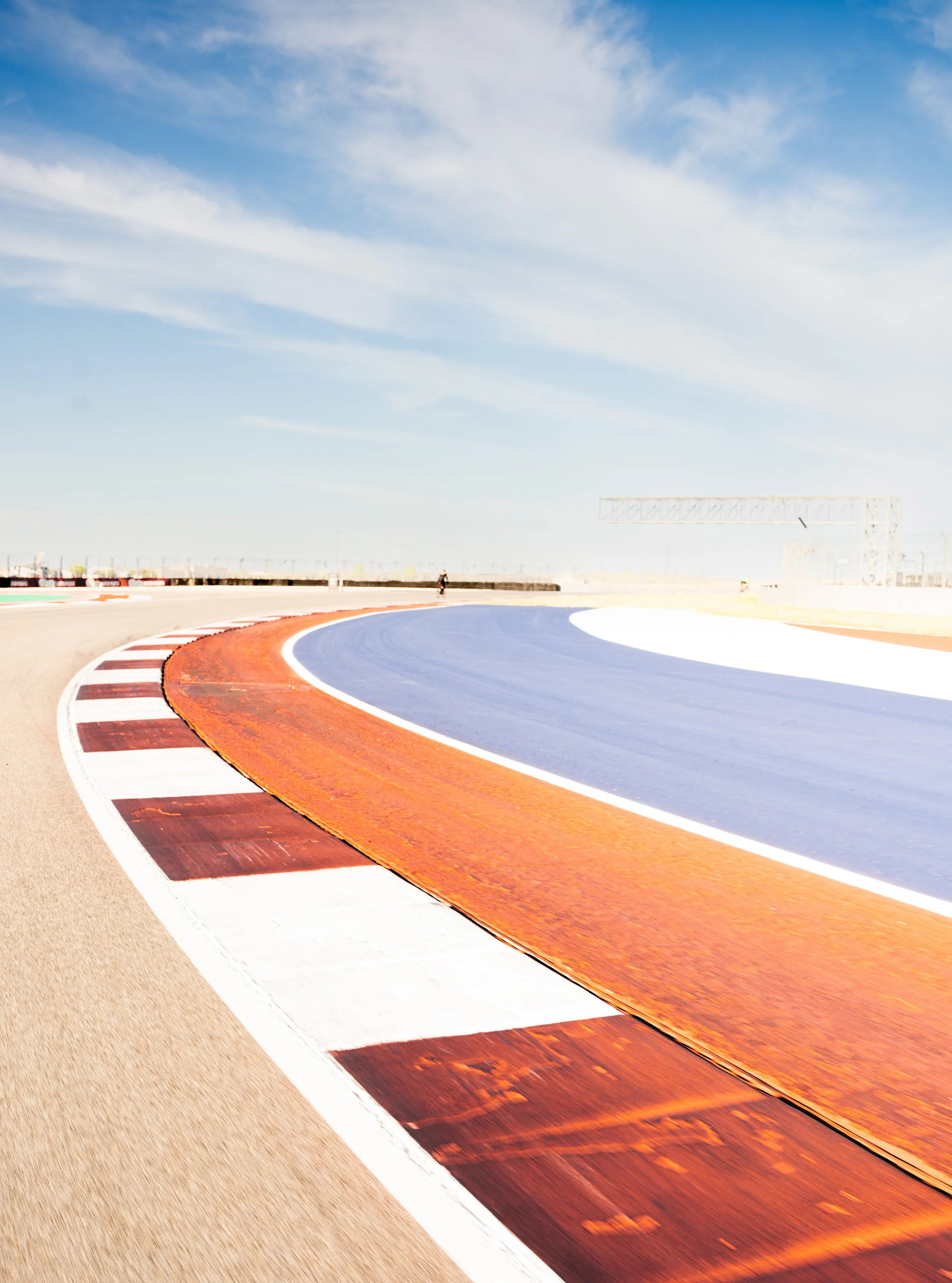 A race track with red, white, and blue painted sections curving in the distance under a partly cloudy sky.