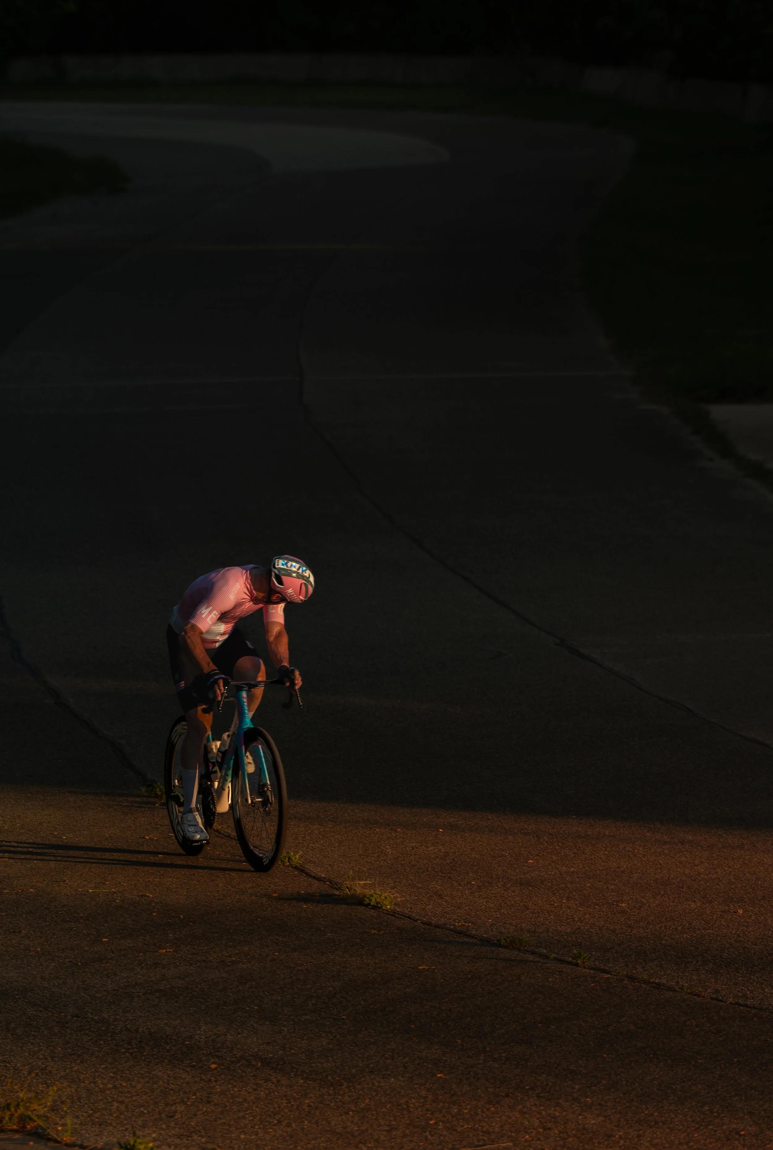 A cyclist riding on a dark road during low light conditions, wearing a helmet and athletic clothing.