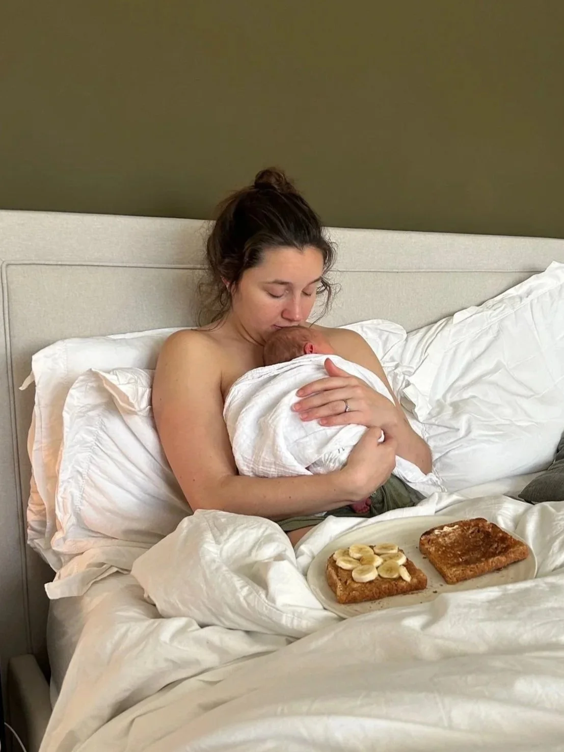 Alice cuddling her newborn daughter in bed, with a good supply of peanut butter and banana on toast.