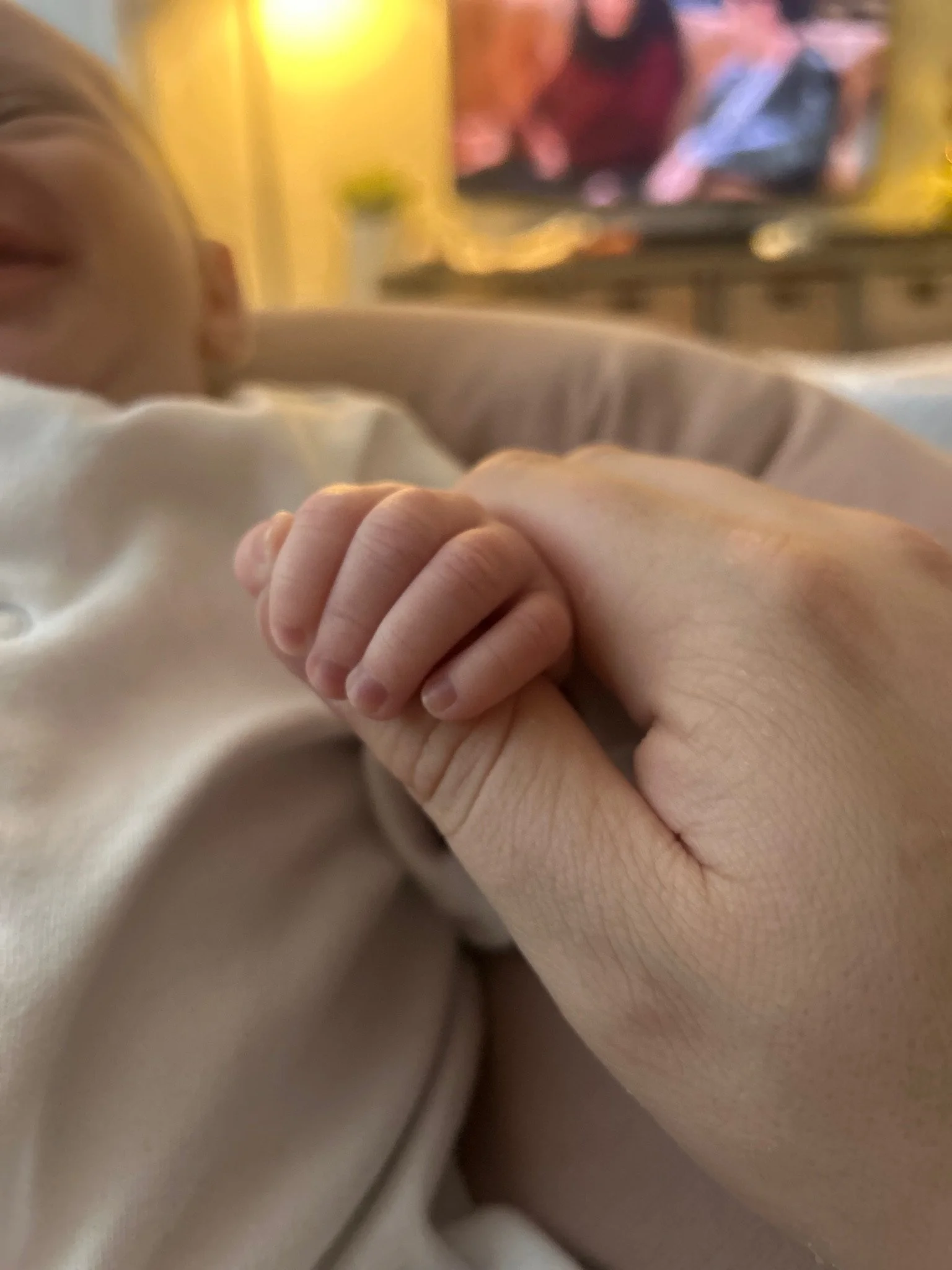 A close-up of a child's hand holding an adult's hand in a warm, intimate moment.