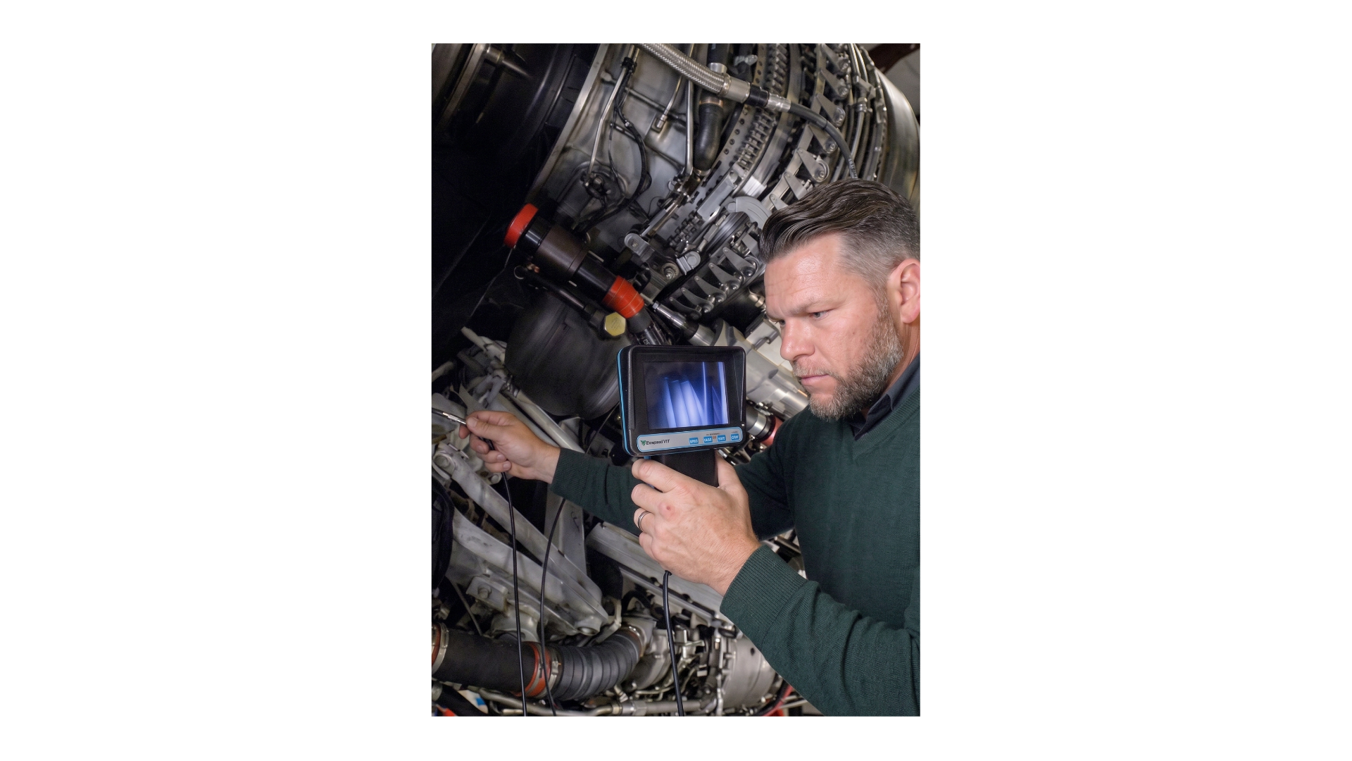 A man with gray hair and beard inspecting an aircraft engine using diagnostic equipment.