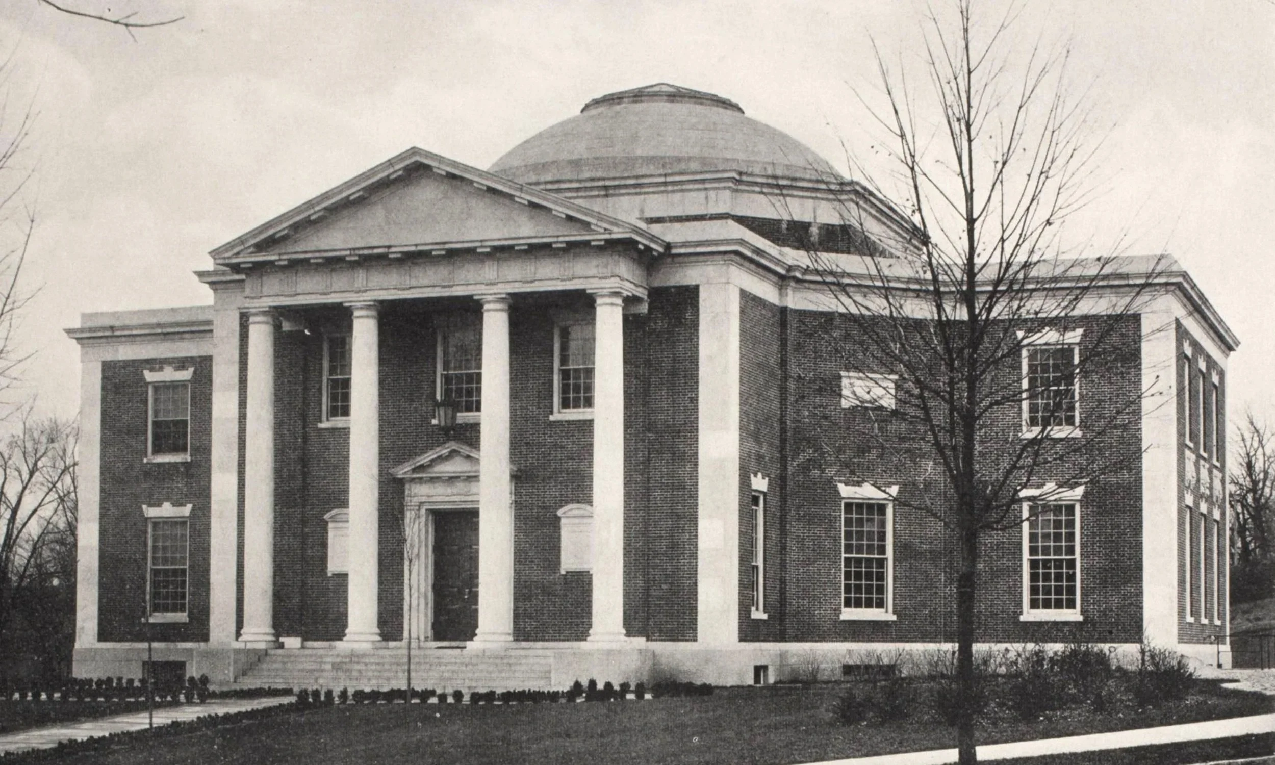 A black-and-white photo of a large, historic brick building with classical columns and a domed roof, set against bare trees and a clear sky. American Antiquarian Society, Worcester, Massachusetts