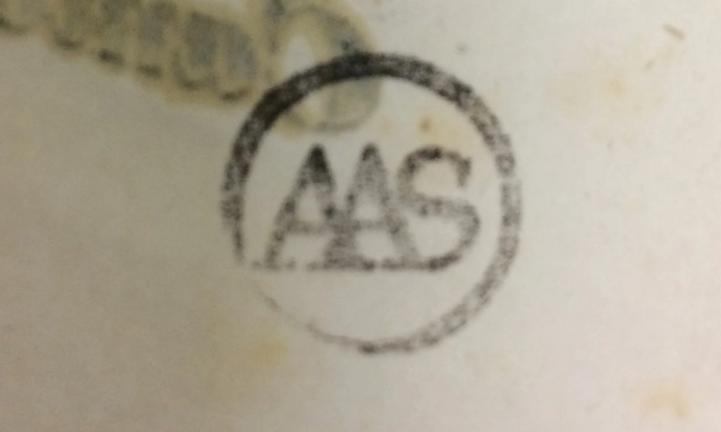 Close-up of a circular stamp with the letters and numbers 'AAS' in the center, on a surface with some discoloration.