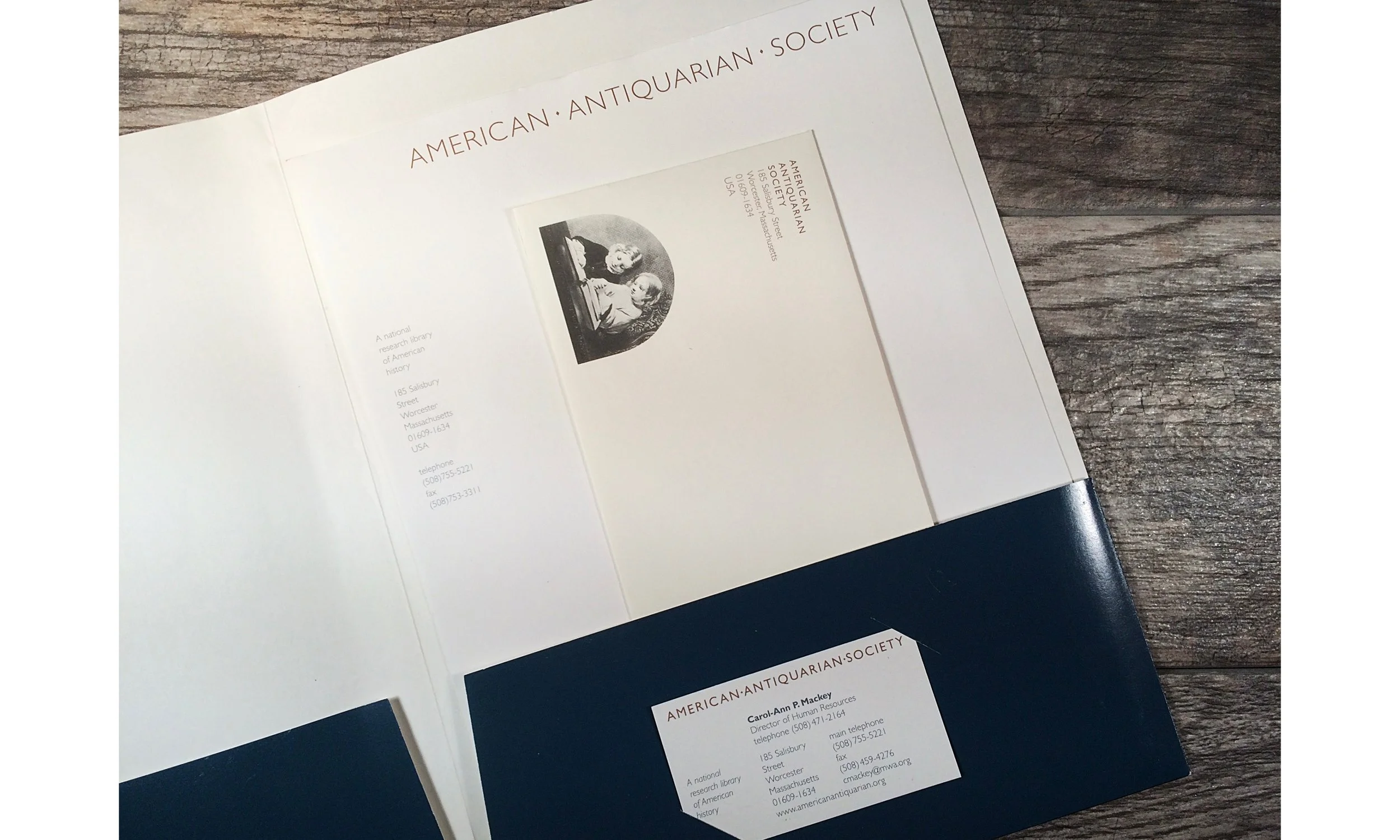 Pamphlet or brochure for the American Antiquarian Society on a wooden surface, with part of a dark blue folder visible at the bottom.