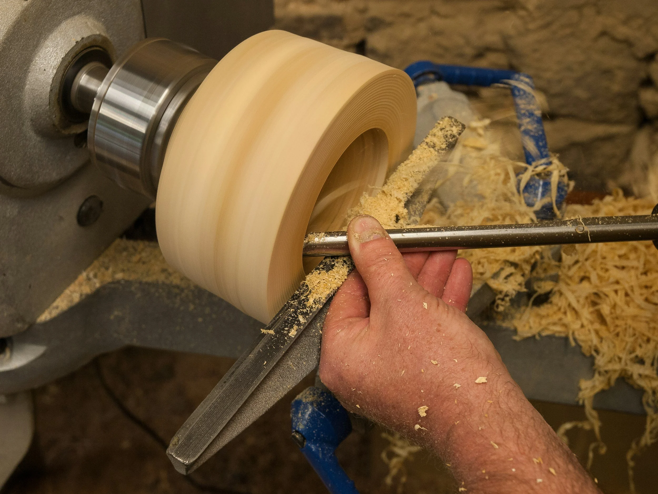 Ein Handwerker nutzt eine Drechselbank. Die Maschine läuft, und es sprühen Holzspäne umher.