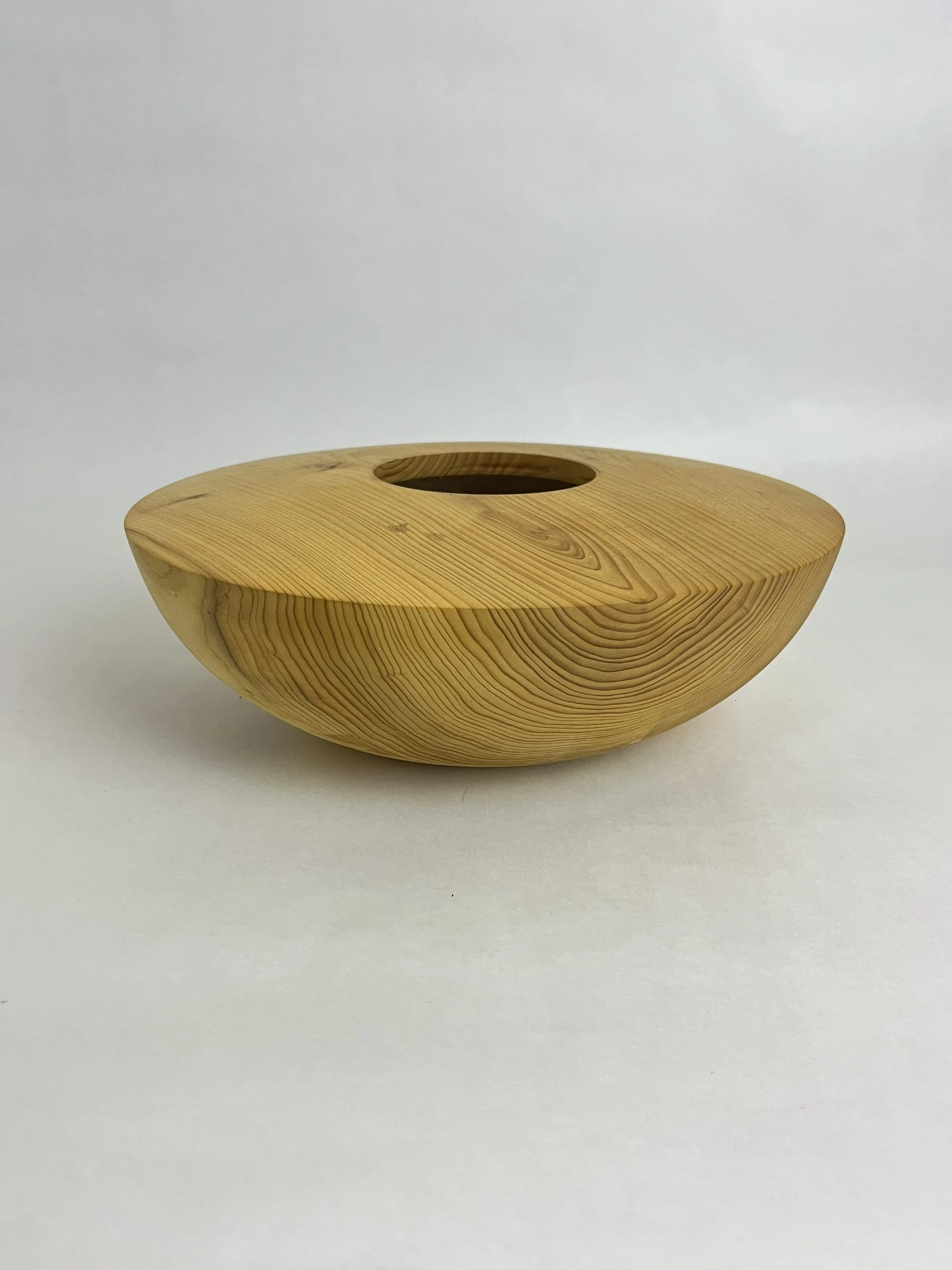 Ein runder, aus hellem Holz gefertigter Behälter mit einem runden Loch in der Mitte, auf weißem Hintergrund.