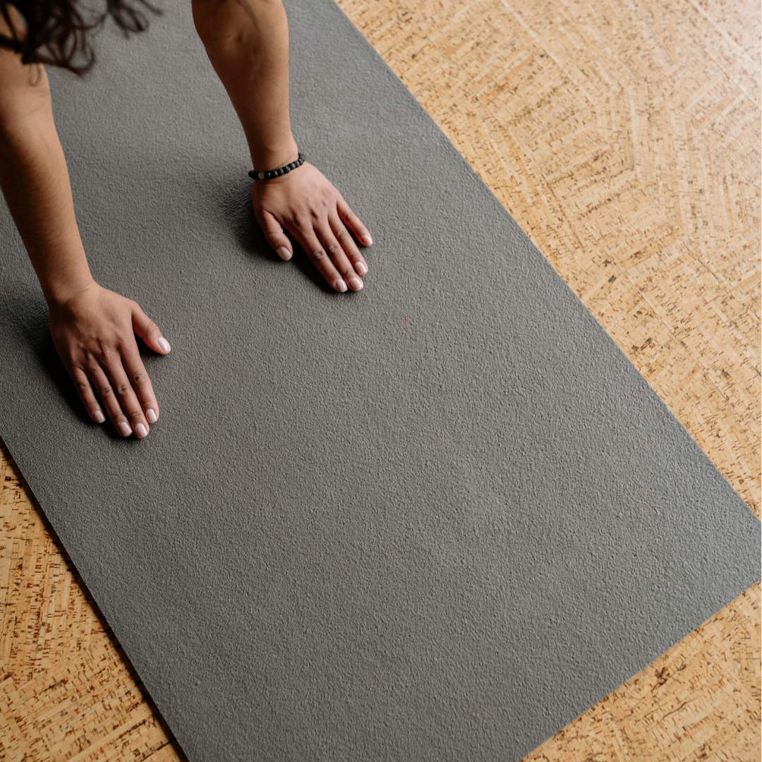 Person in a black beaded bracelet doing a plank exercise on a gray yoga mat on a wooden floor.