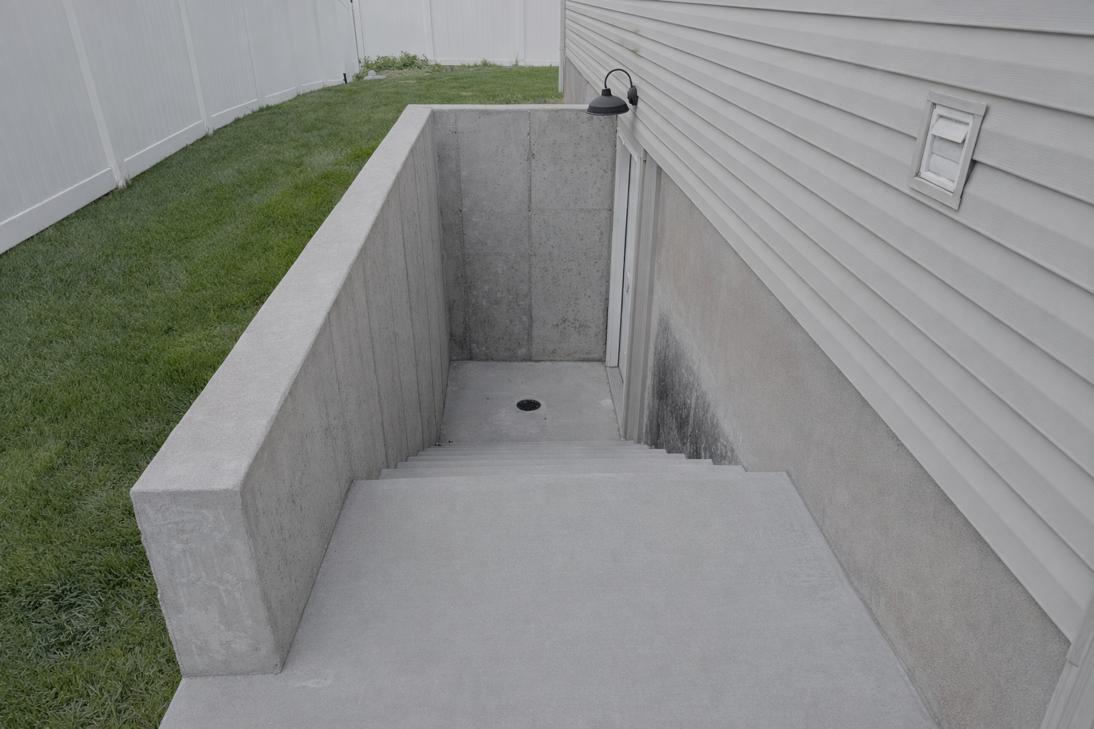 Concrete basement staircase and yard with white fencing