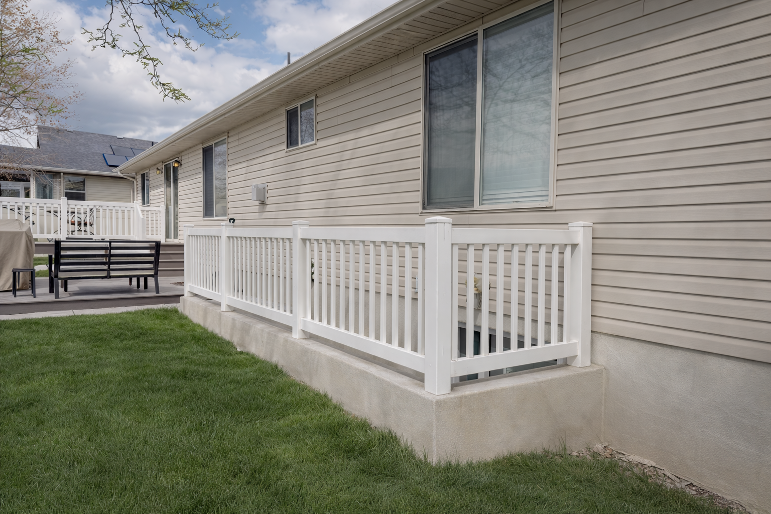 Backyard with a white safety railing, grassy lawn, and a beige house with sliding glass doors and windows.