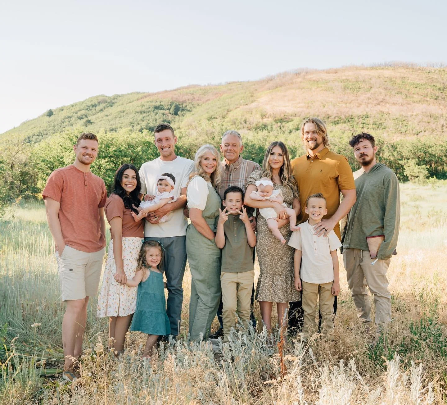 Family group outdoor photo in a field with green hills in the background on a sunny day.