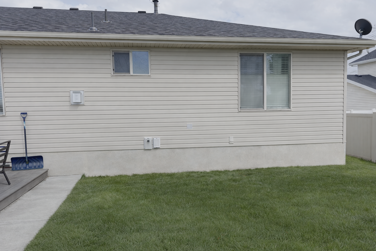 Backyard view of a white house with vinyl siding, a small porch with steps, a blue snow shovel leaning against the porch, and a grassy lawn.