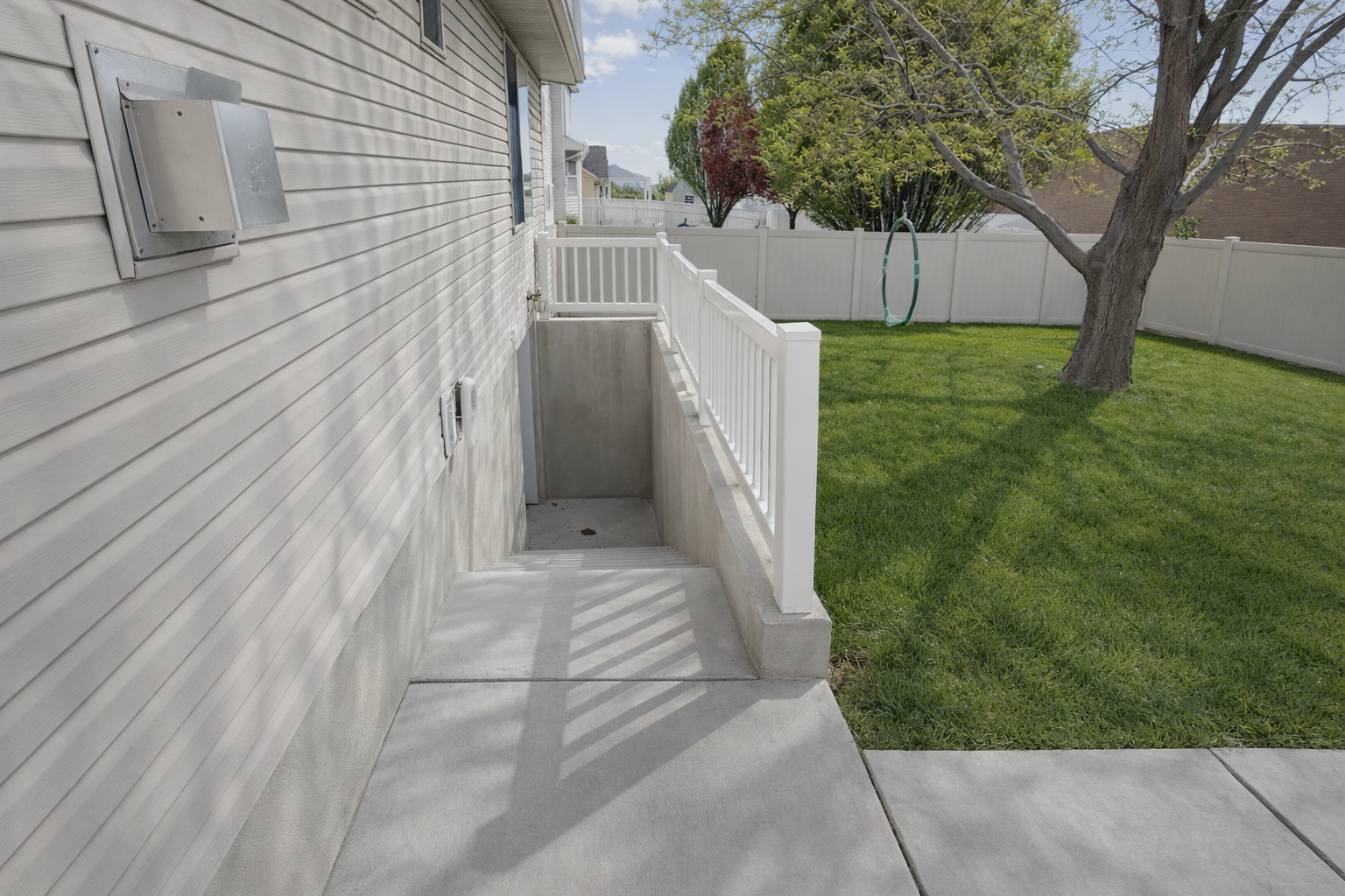 Backyard with concrete patio, white fence, green grass, tree, and a garden hose.