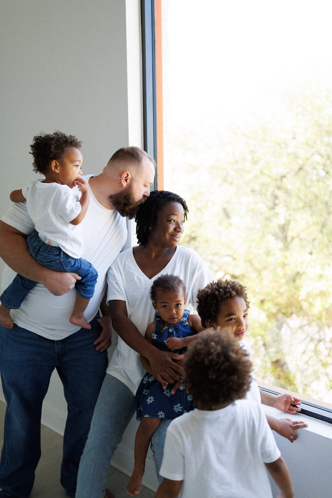 Family looking out a large window on a sunny day, children and adults together