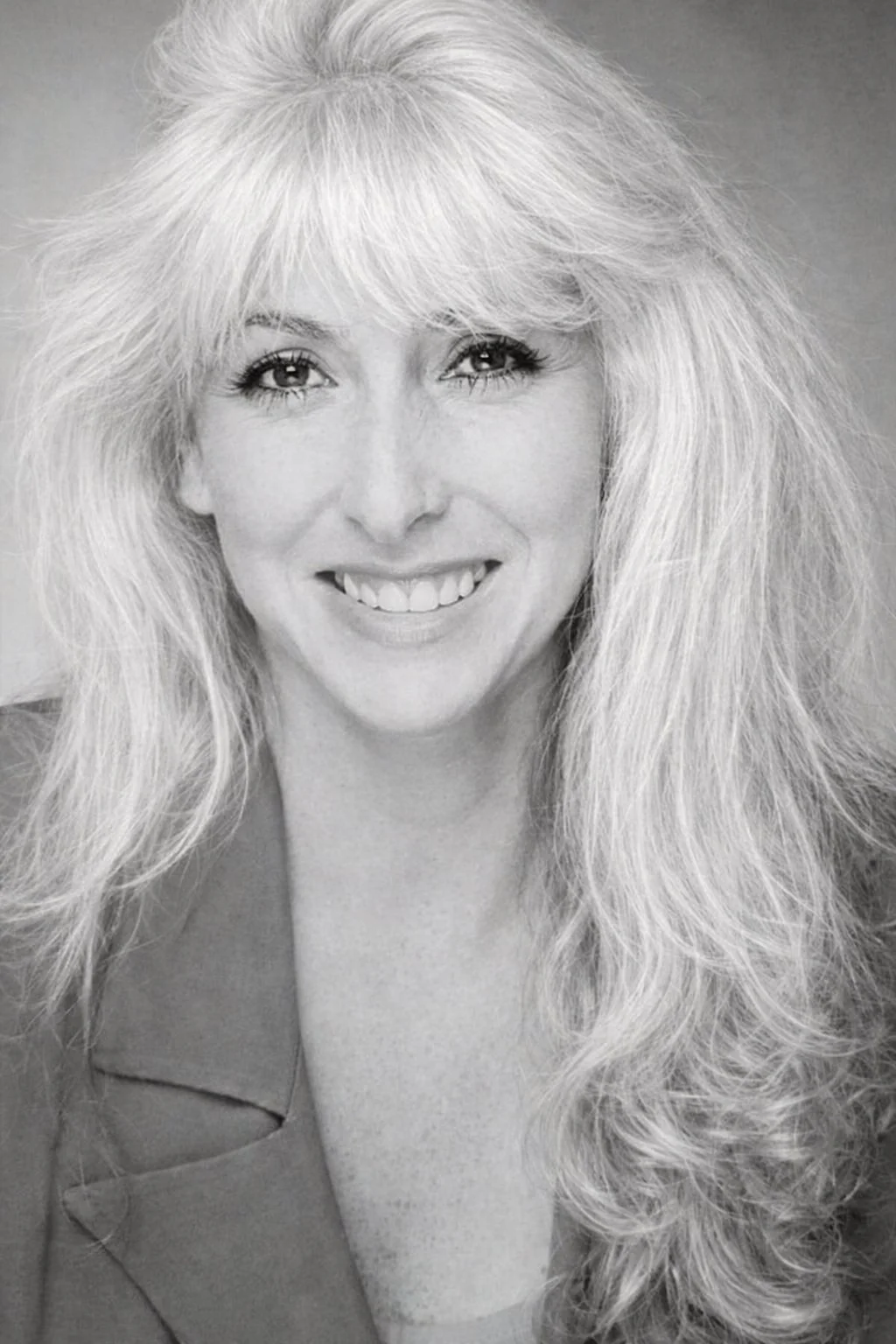 Black and white portrait of a woman with voluminous, layered hair smiling at the camera.