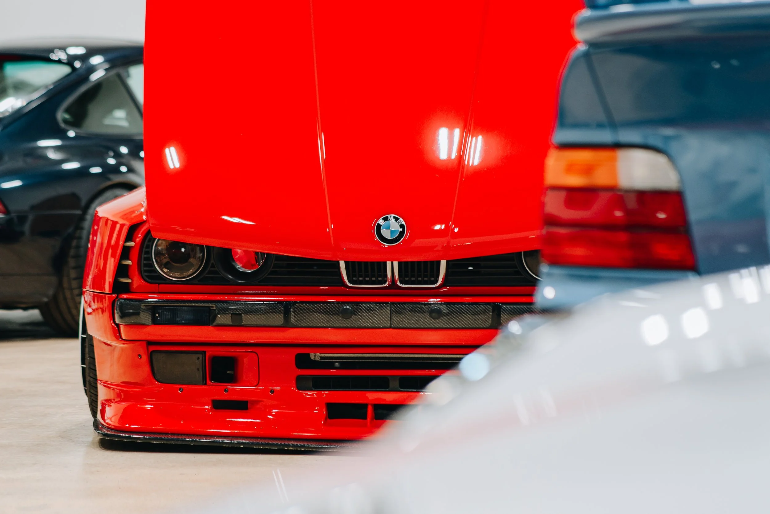 Front view of a red BMW car with a hood ornament, parked indoor with other cars visible in the background.
