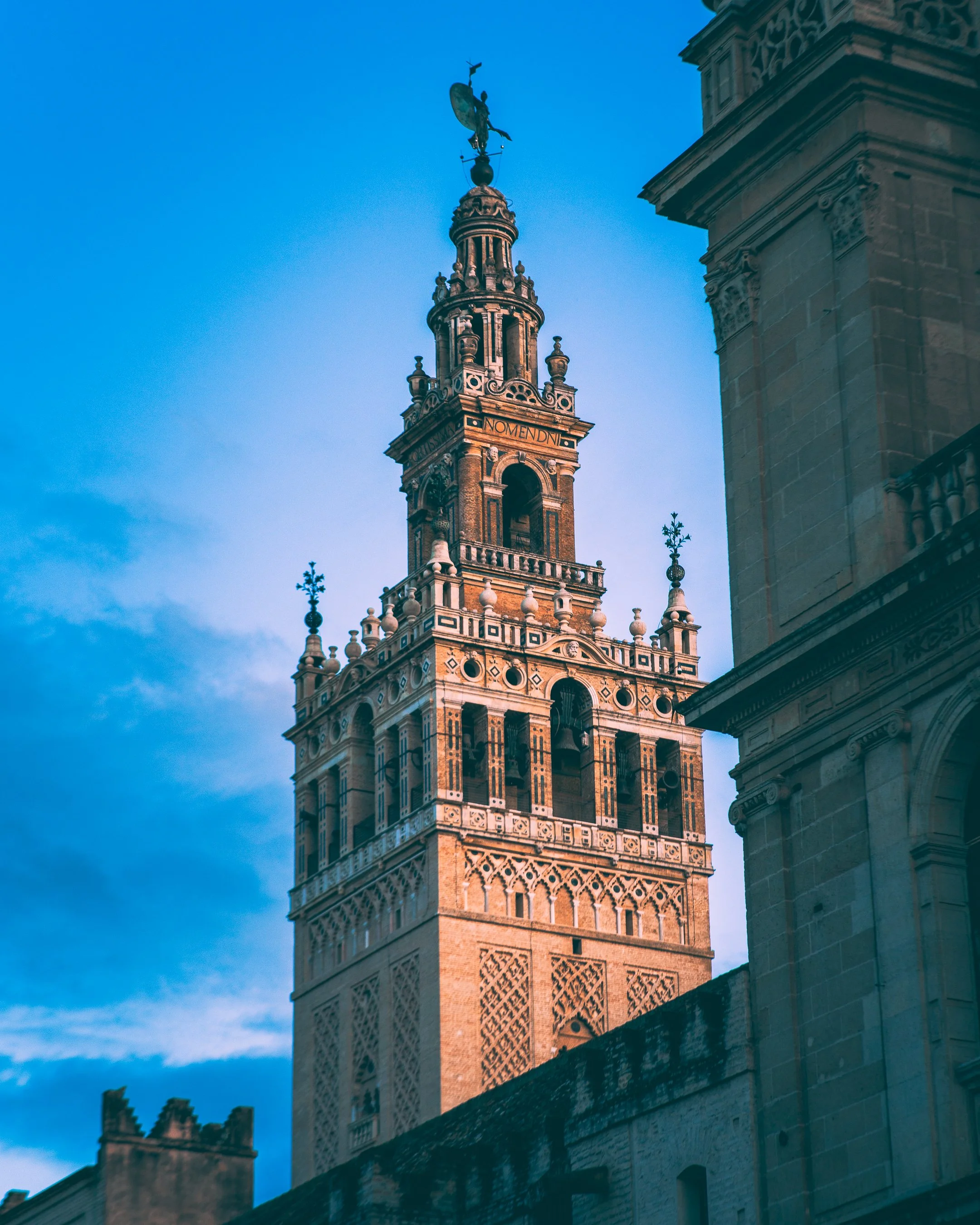 Historic tower with ornate architecture, topped by a weather vane, under a blue sky.