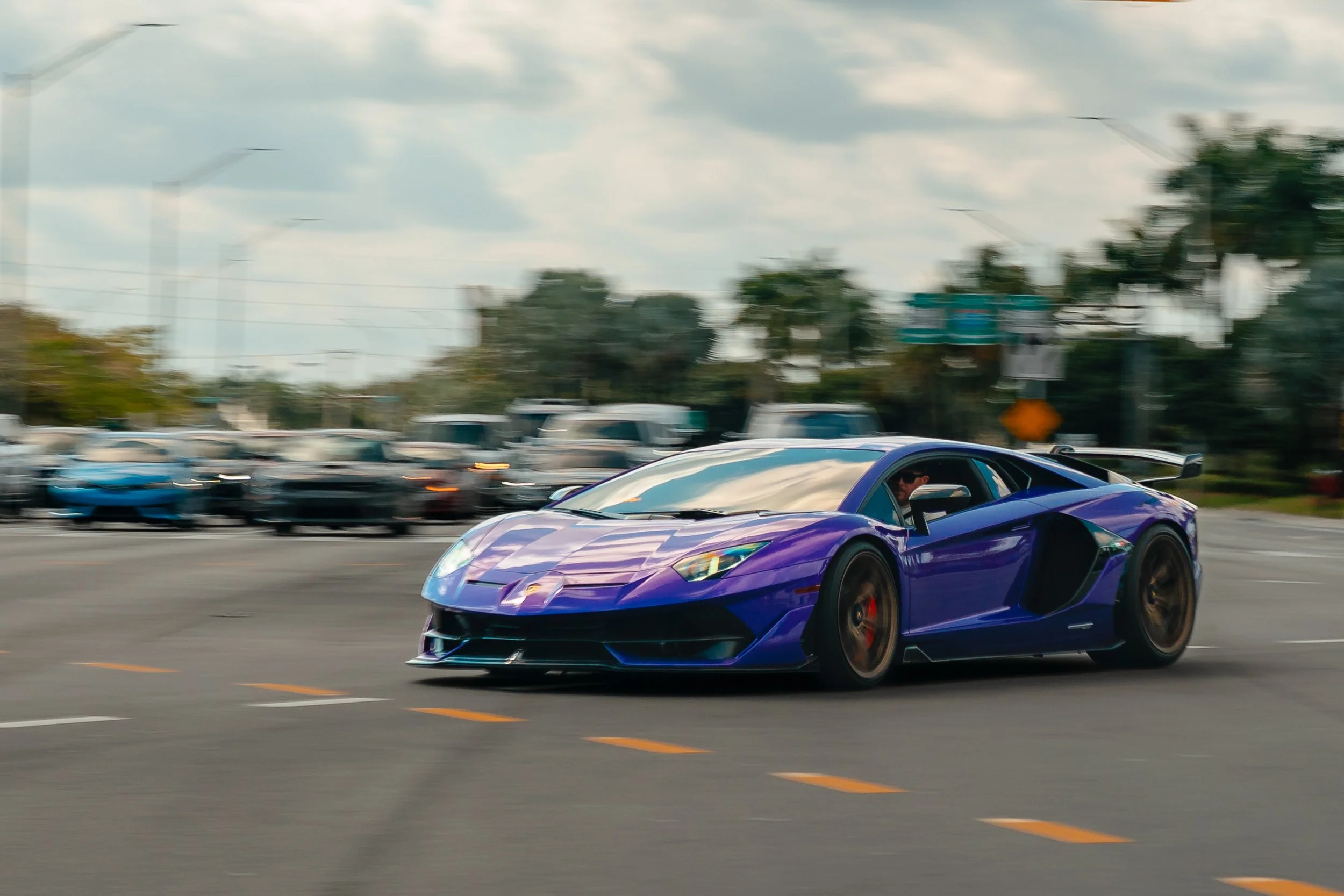 A purple Lamborghini sports car speeding on a city street, with a blurred background of other vehicles and trees.