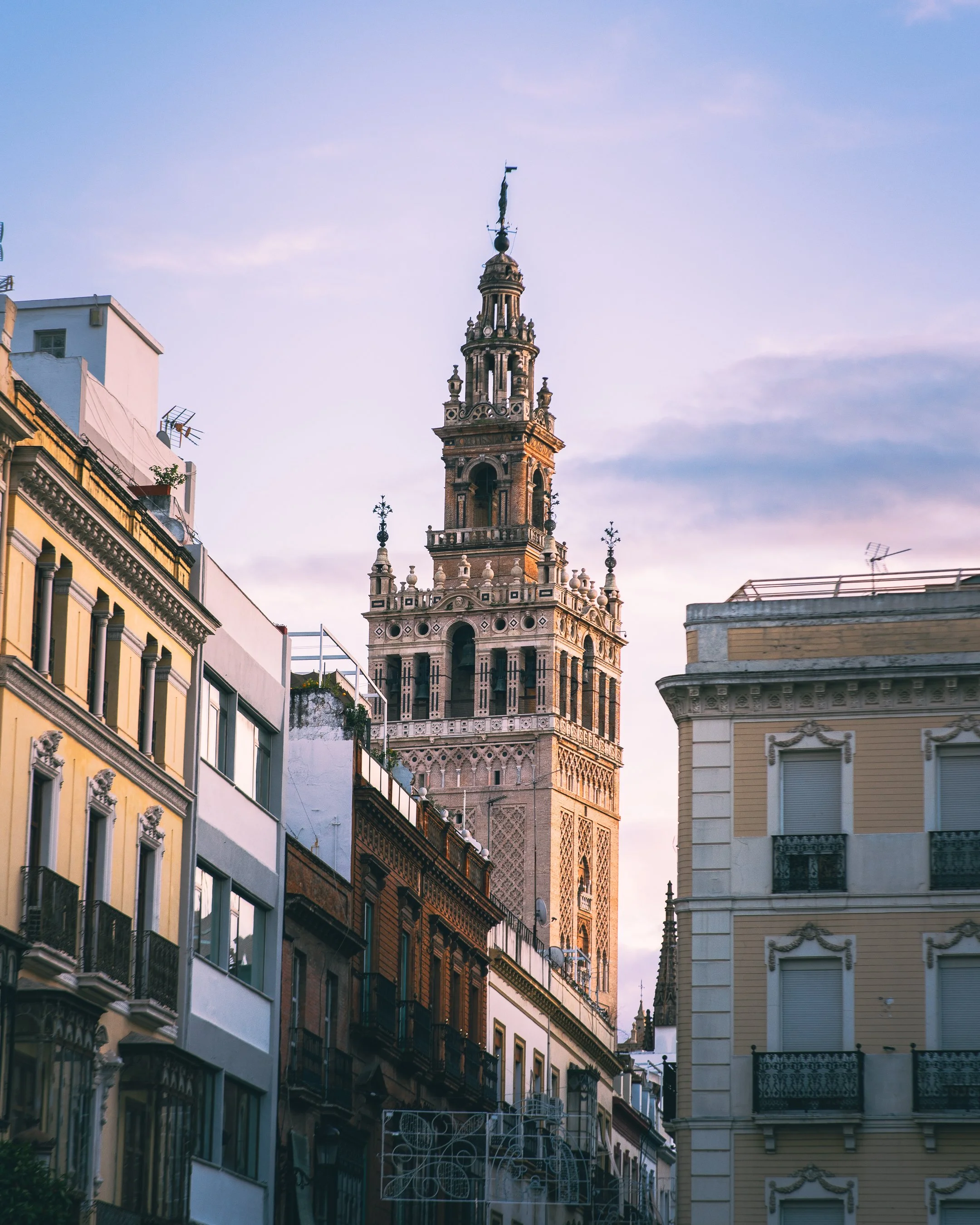 Cityscape with a historic clock tower in the background and colorful buildings in the foreground during sunset.