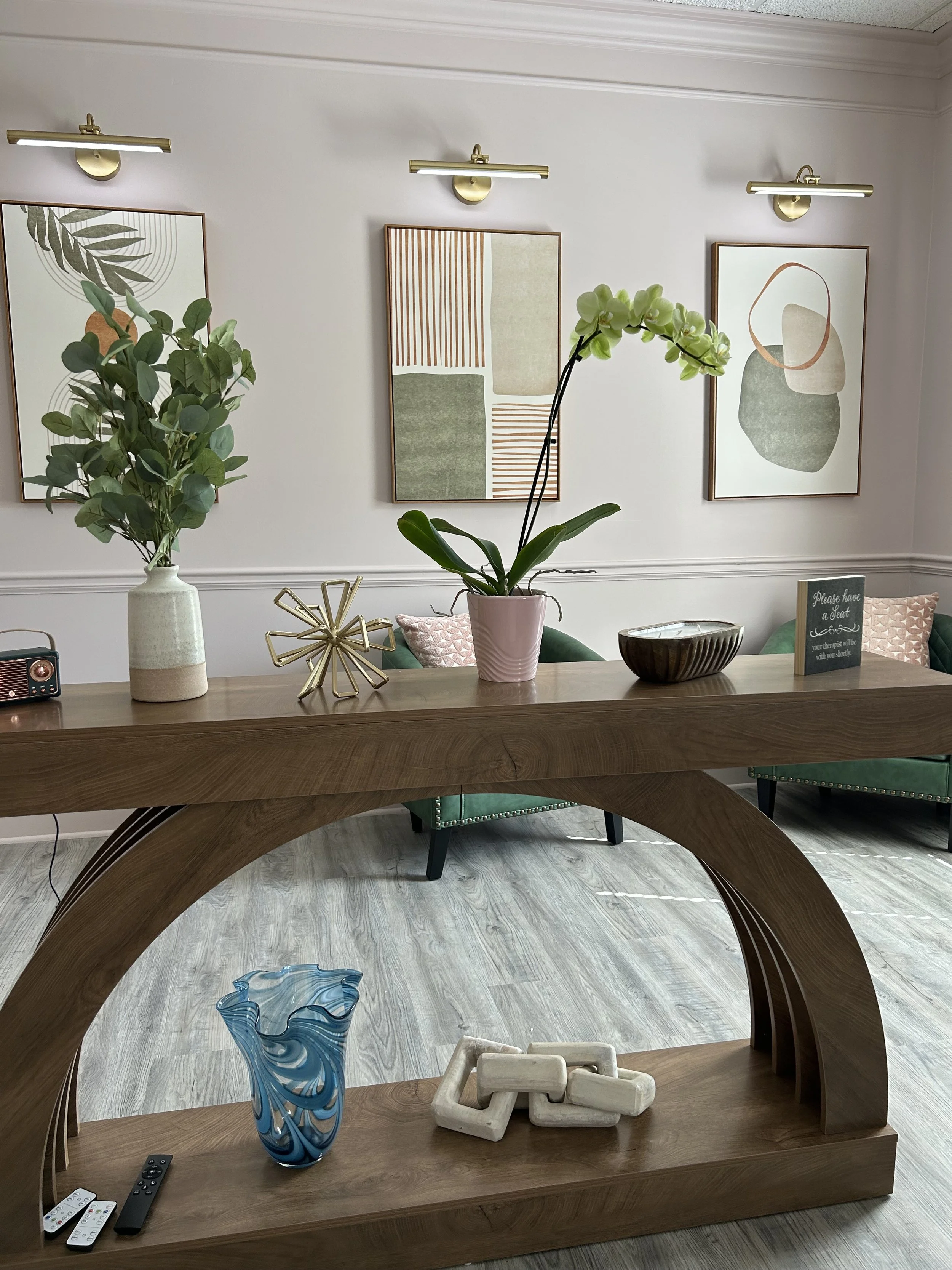 Living room decor with a wooden coffee table, decorative vases, a potted orchid, abstract wall art, and a bookshelf.