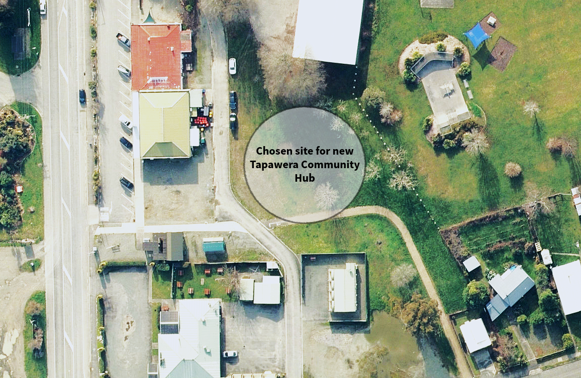 Aerial view of a neighborhood with residential houses, green lawns, trees, and parks. A large circular area is marked as the site for a new Tapawera Community Hub.