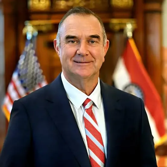 Missouri Governor Mike Kehoe. A middle-aged man in a navy suit, white shirt, and red striped tie, standing in front of American and Missouri state flags in a formal setting.