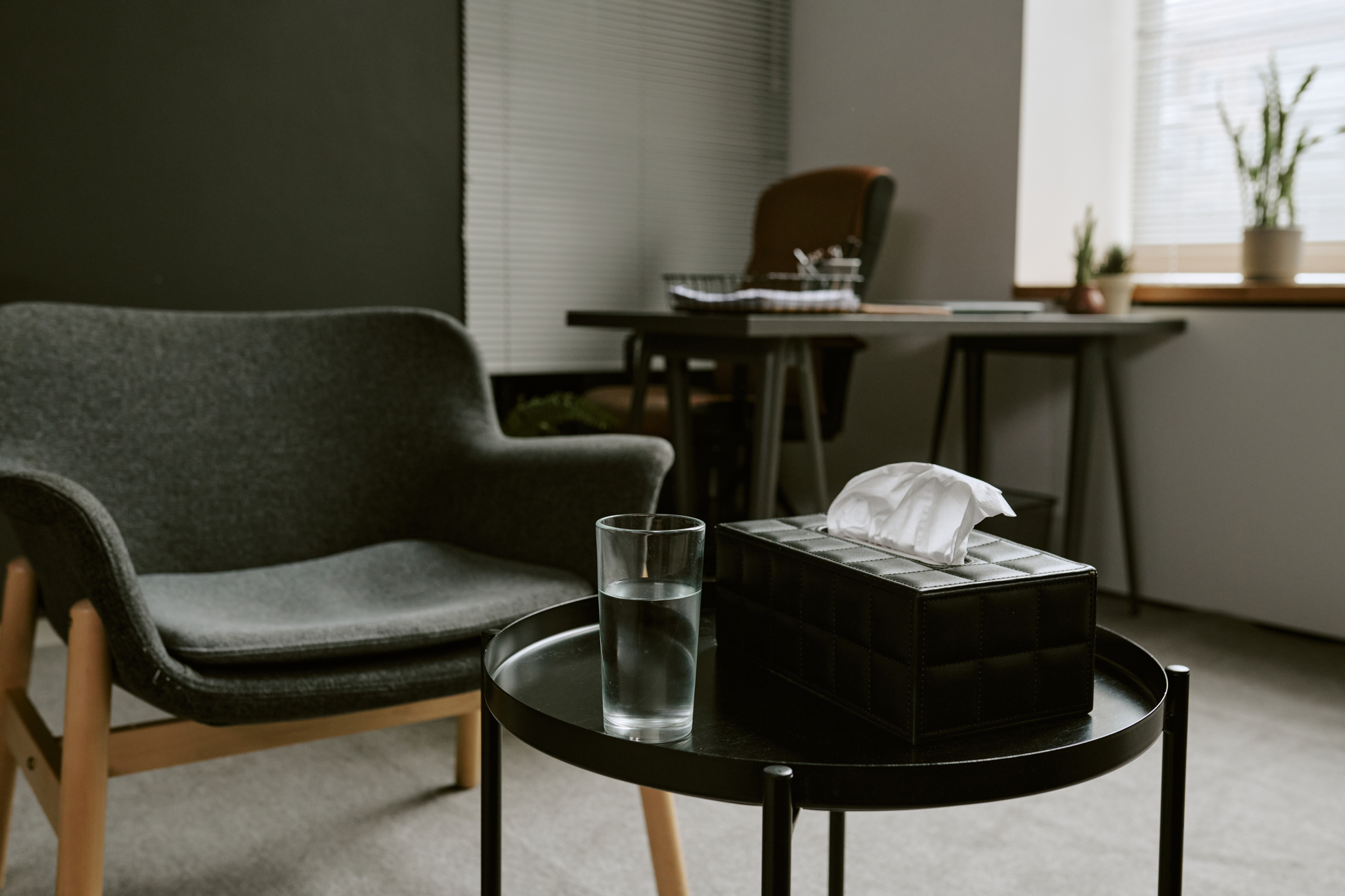 An empty consultation room with an armchair, tissue box, and glass of water.